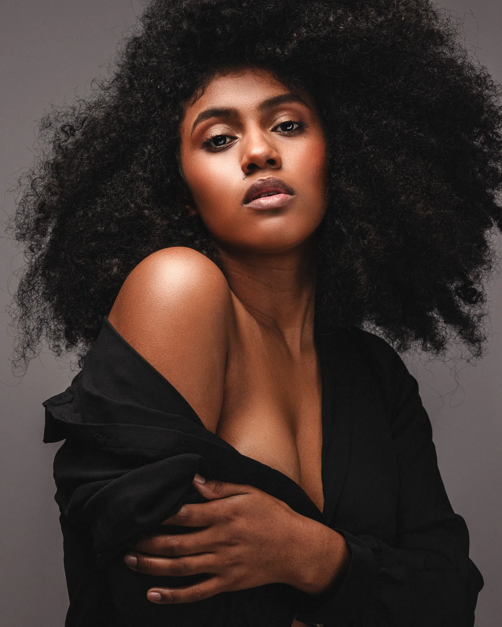 Portrait of a woman with natural hair in a black open shirt against a grey background