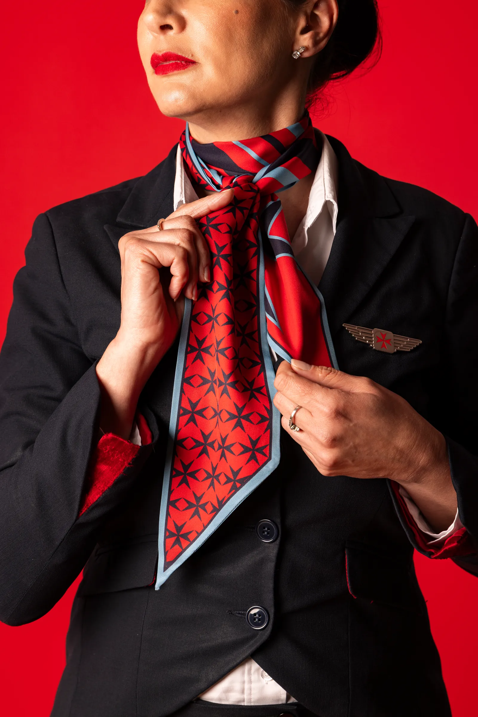 KM Malta Airlines flight attendant tying a Charles & Ron red scarf against a red background