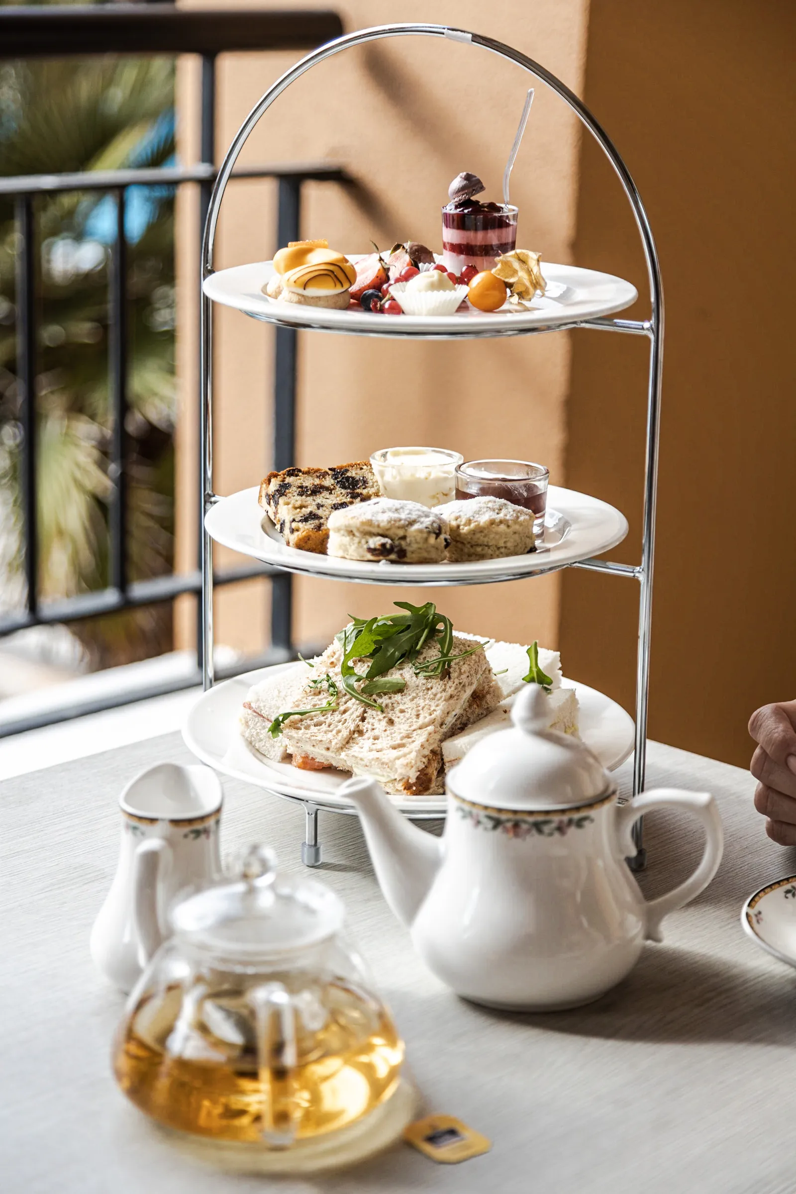Three-tier stand of afternoon tea pastries with teapots on a balcony table
