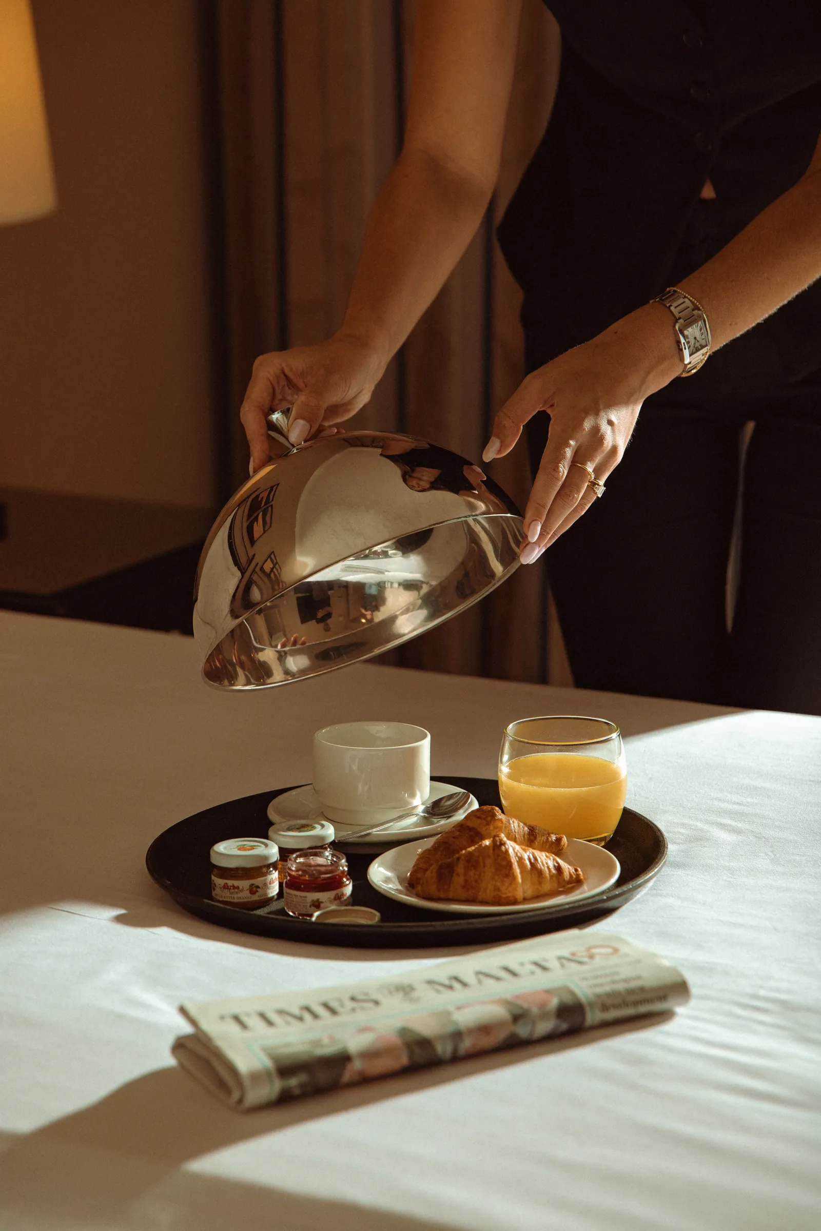 Breakfast tray with croissant, juice and a silver pot on the bed, Corinthia Hotels