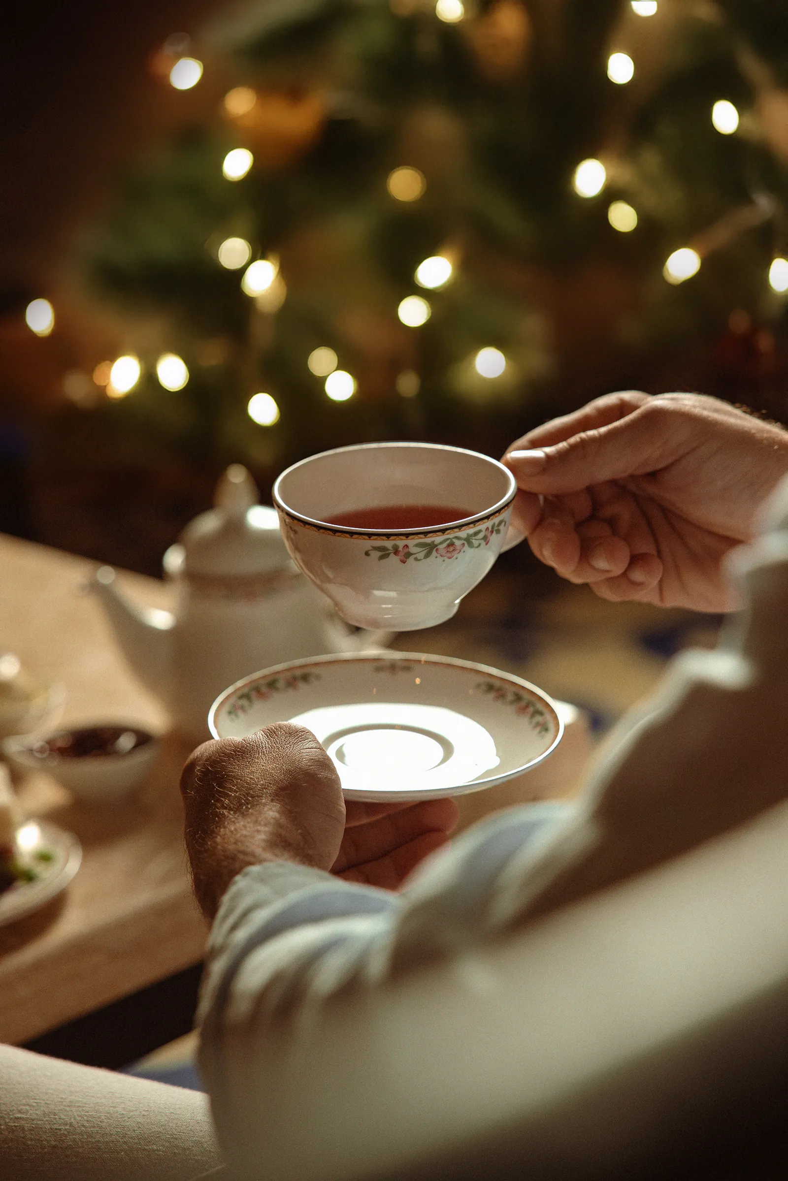 Teacup lifted at a table with festive lights glowing behind