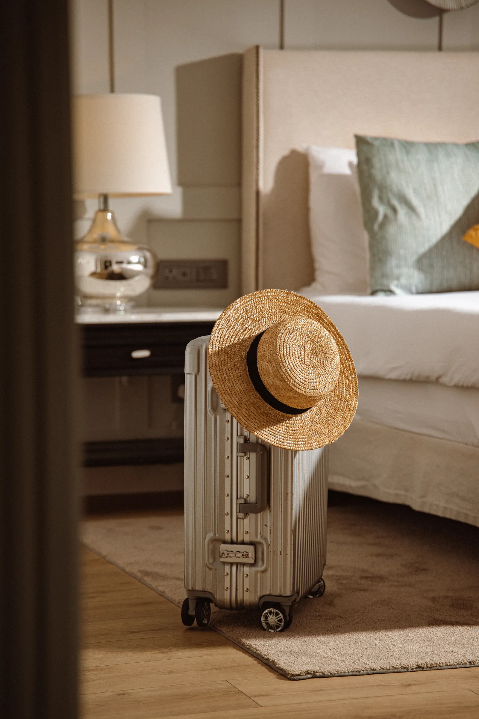 Suitcase and straw hat beside the bed in a Corinthia guest room