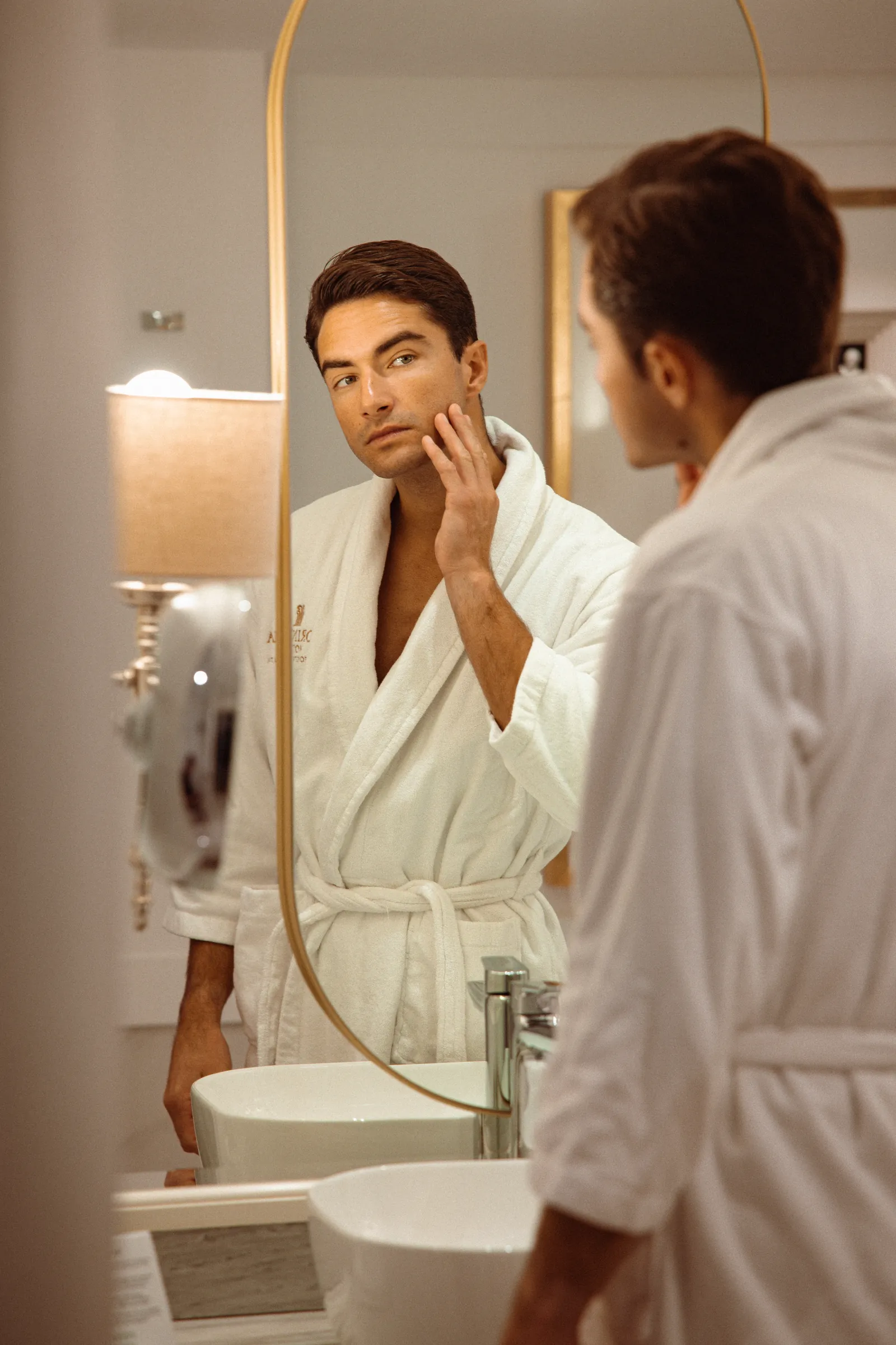 Man in a bathrobe at the bathroom mirror with a second guest, Corinthia Hotels