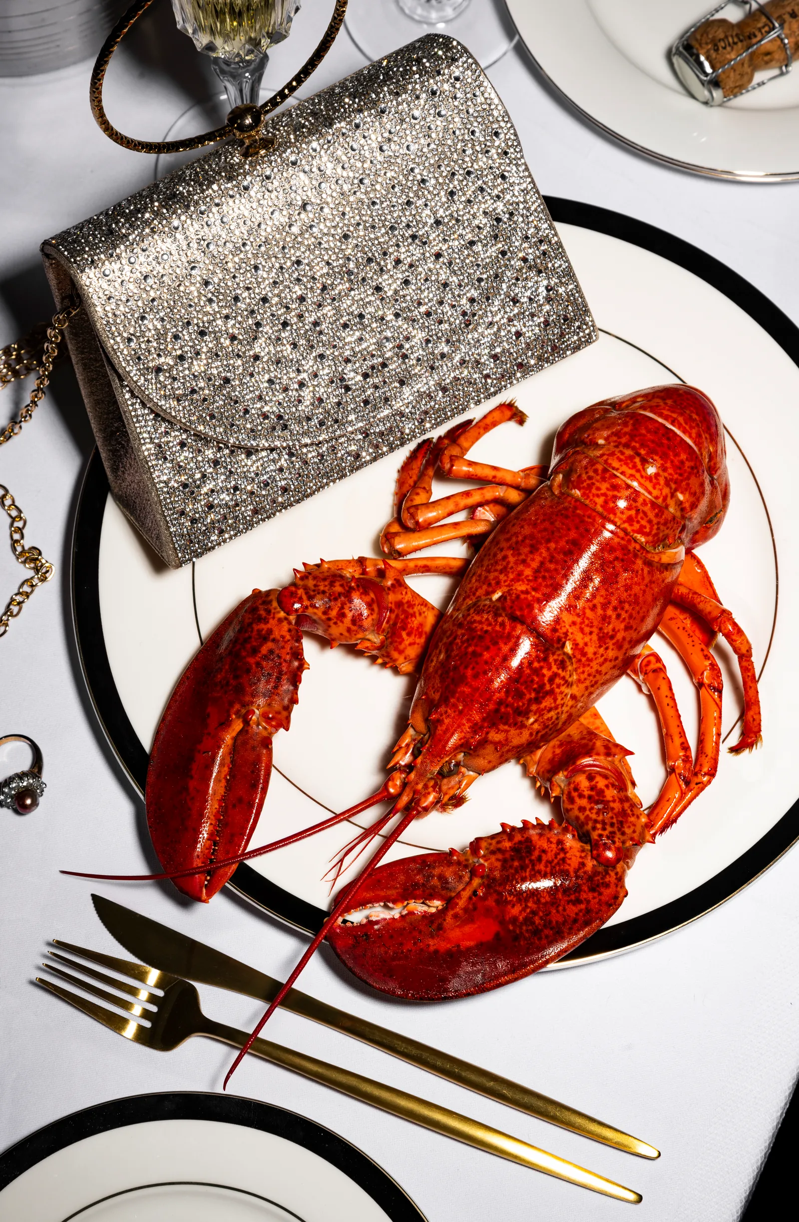 Whole lobster on a plate beside a sparkling clutch bag and cutlery, seen from above