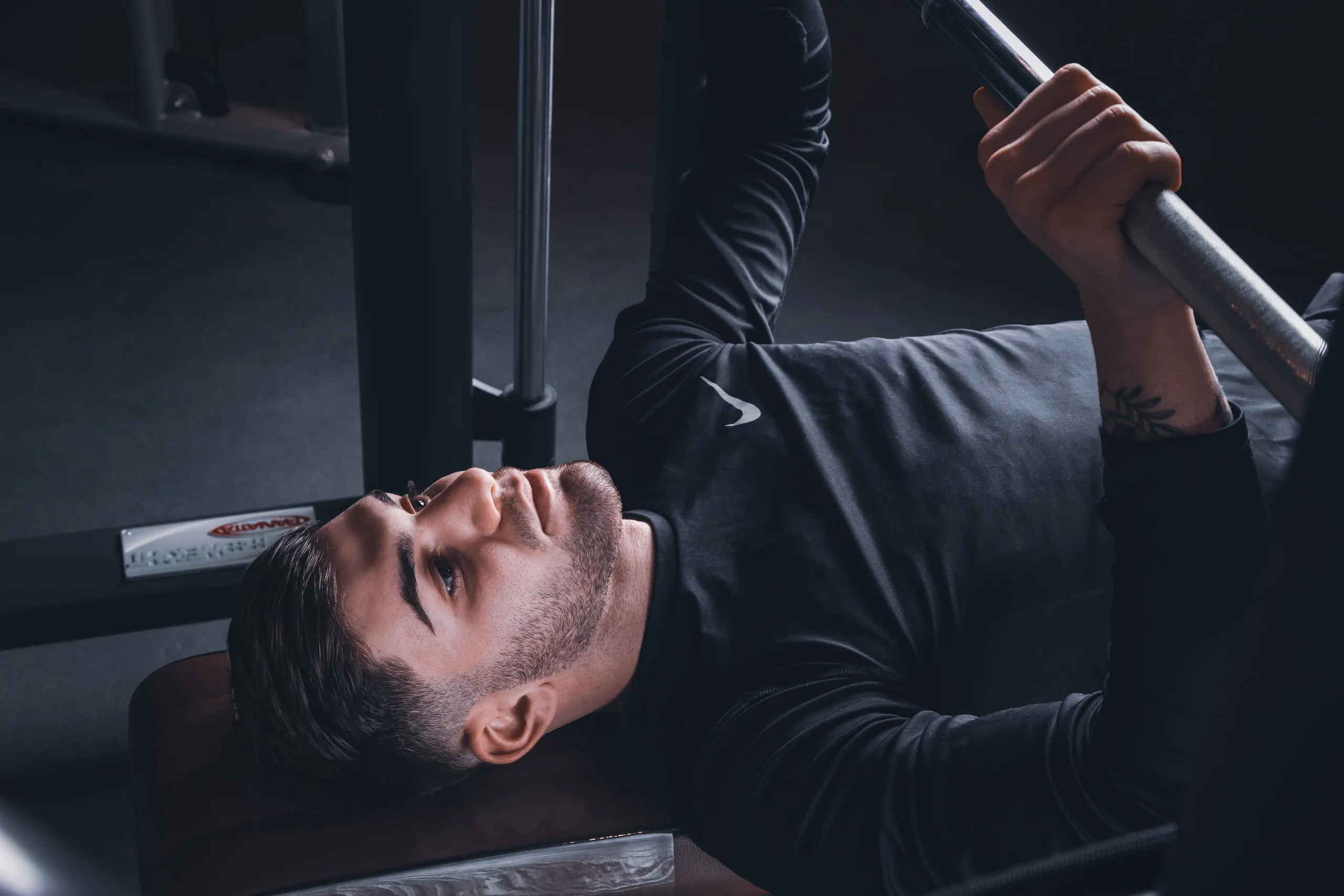 Man lying on a bench lifting a bar in a dark gym