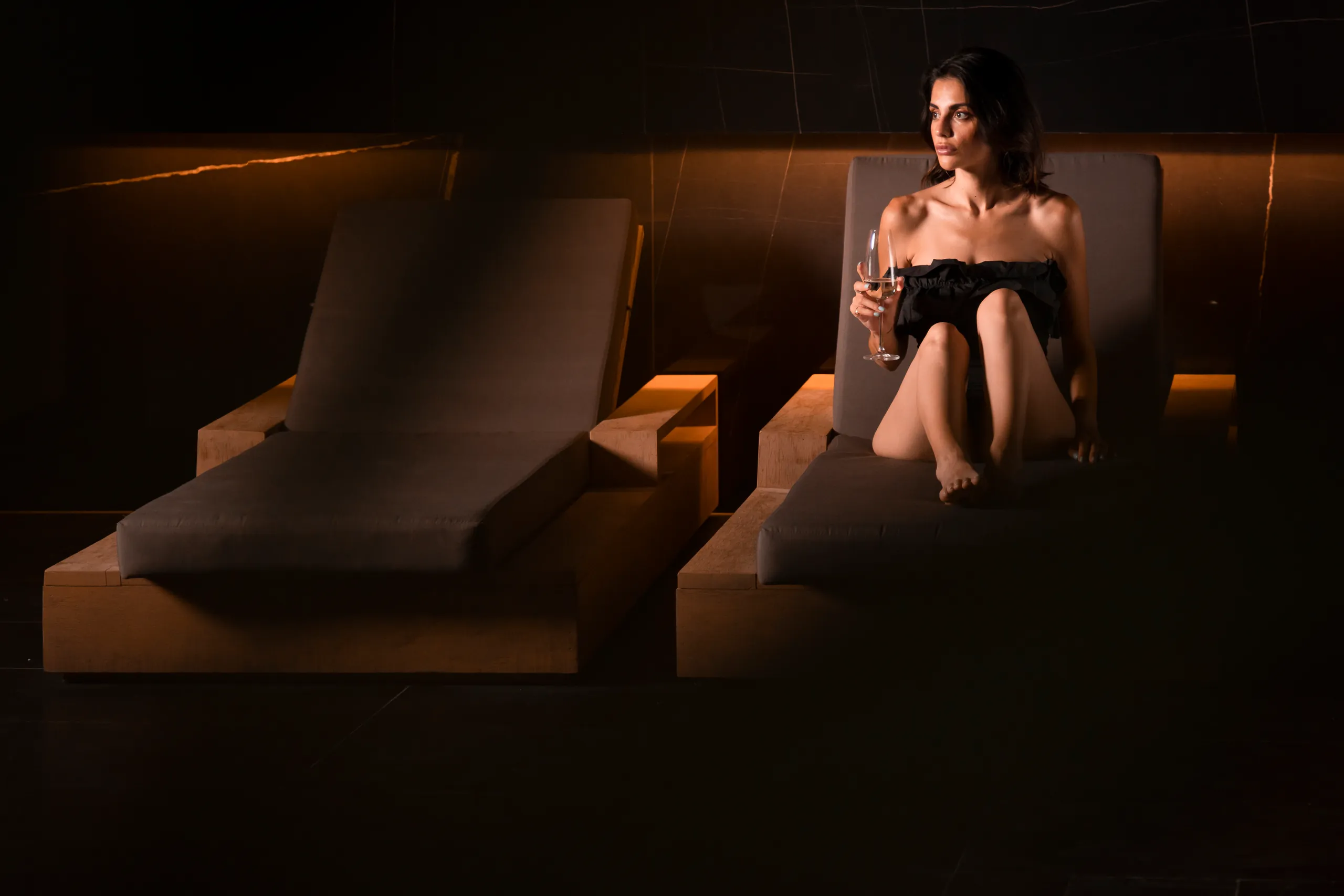 Woman reclining on a lounger in a dim spa relaxation room with warm lighting