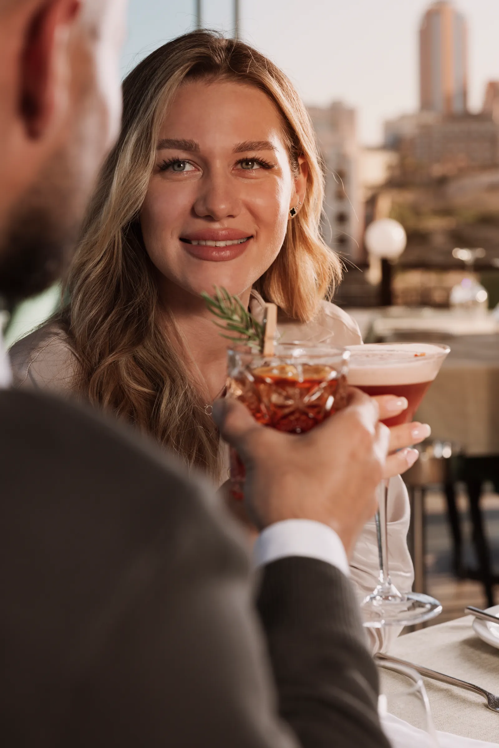 Smiling woman holding a cocktail on a terrace with the city behind