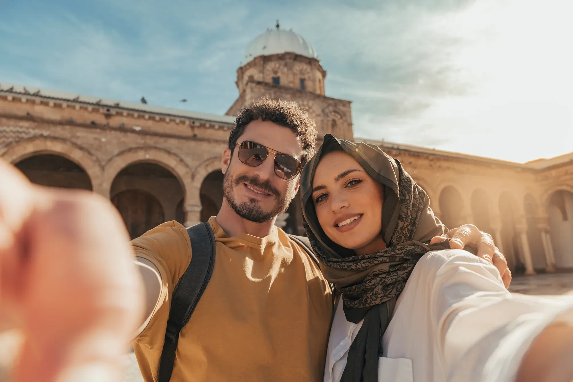 Couple taking a selfie in the sunlit courtyard of a mosque in Tunis