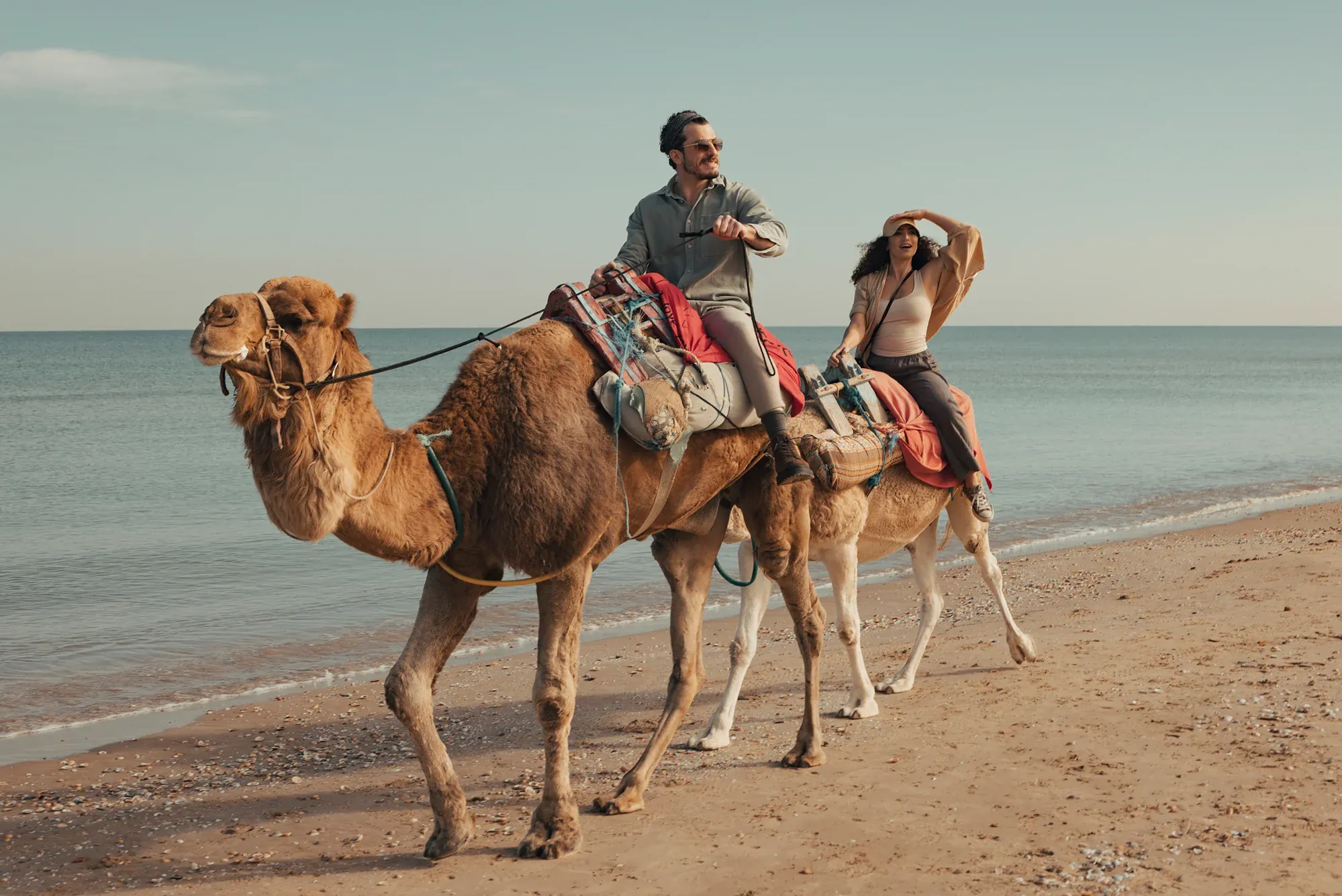 Two camels with riders walking along a beach in Tunisia