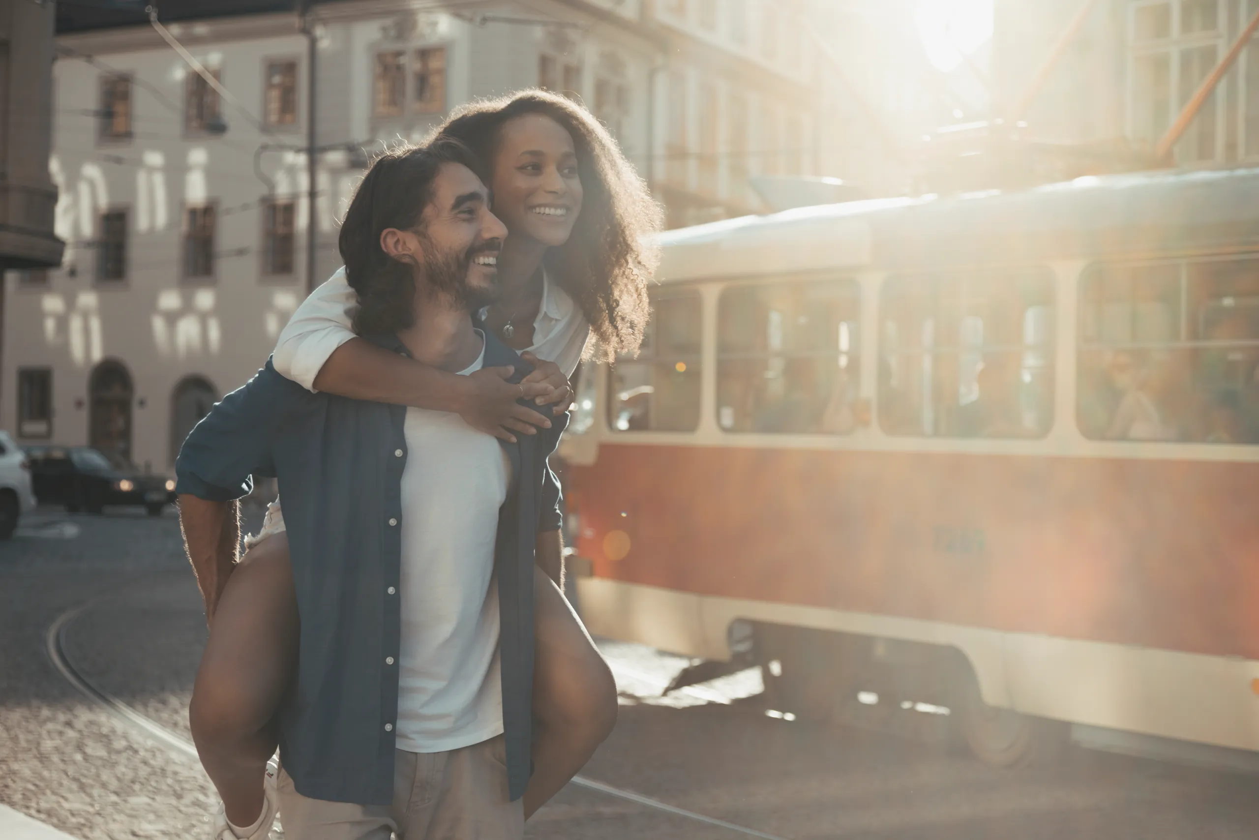 Couple laughing as he carries her piggyback beside a vintage tram