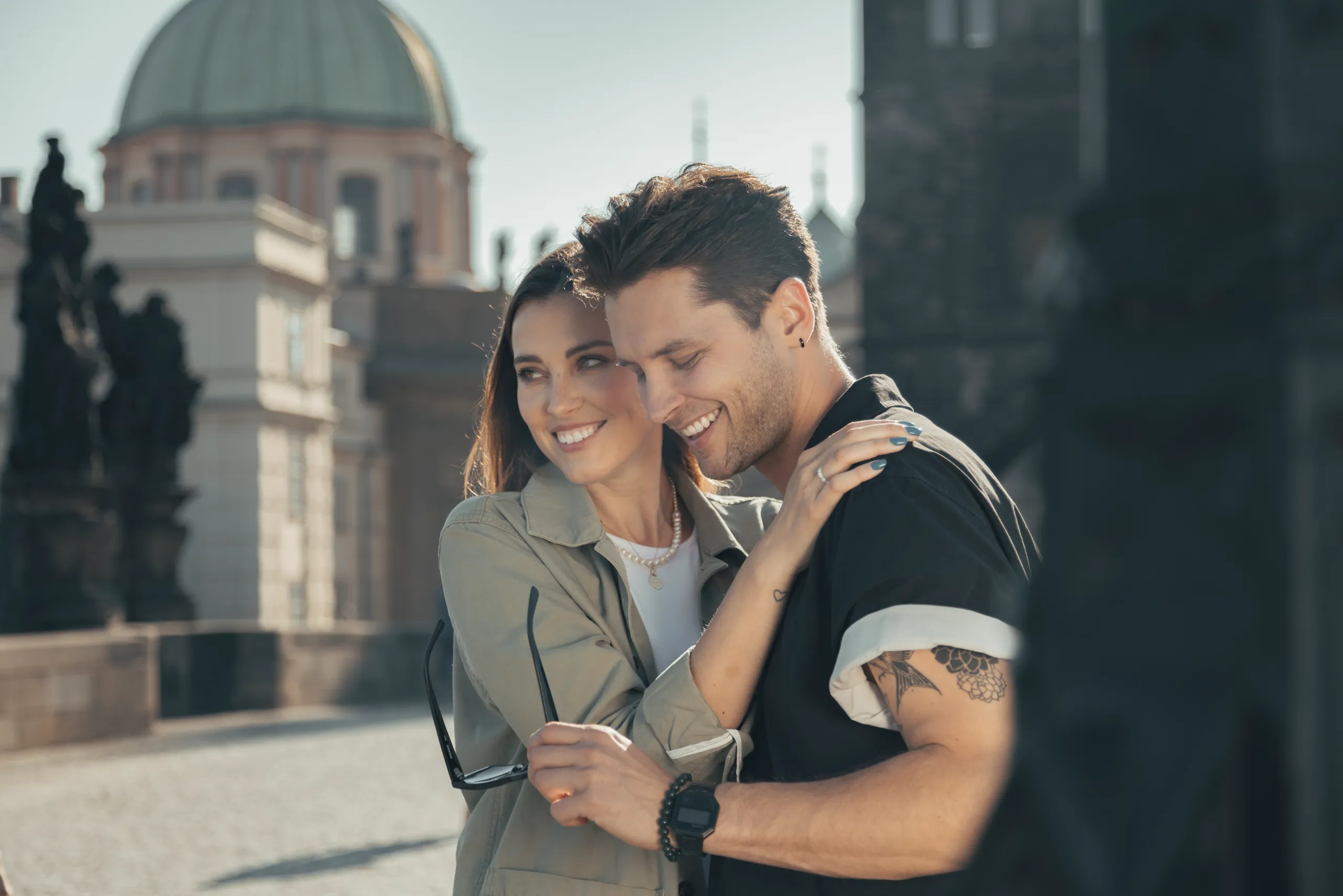 Smiling couple embracing on a cobbled bridge with historic buildings behind
