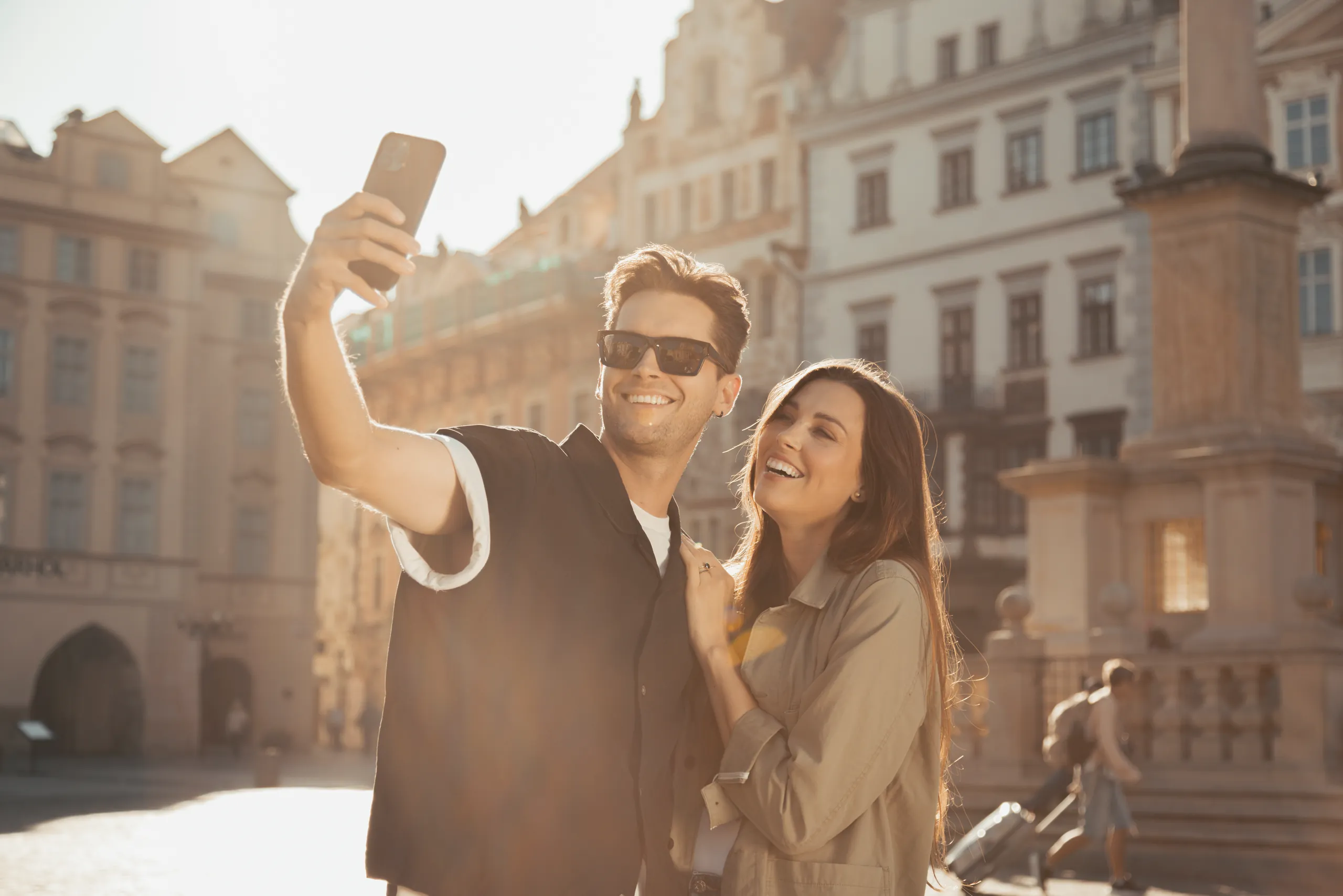 Smiling couple taking a selfie in an old town square in the afternoon light