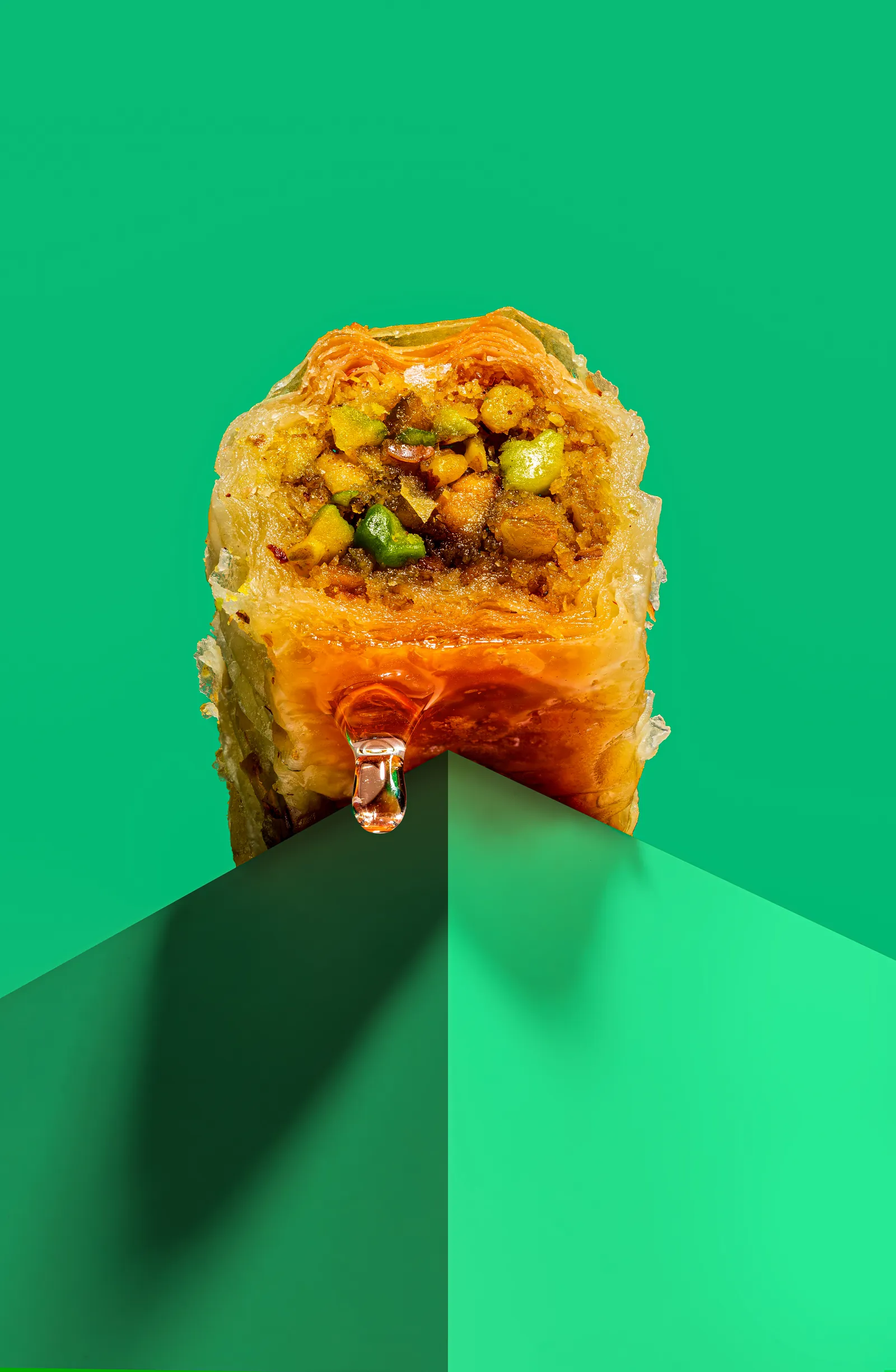 Pistachio baklava cut open with syrup dripping, on green, for Baba Lebanese Street Food