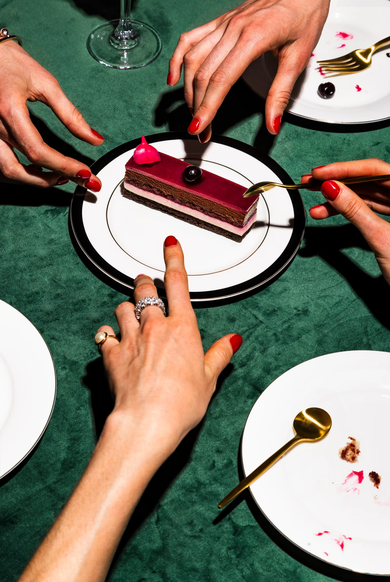 Hands around a table with a slice of chocolate cake on a plate, on a green tablecloth