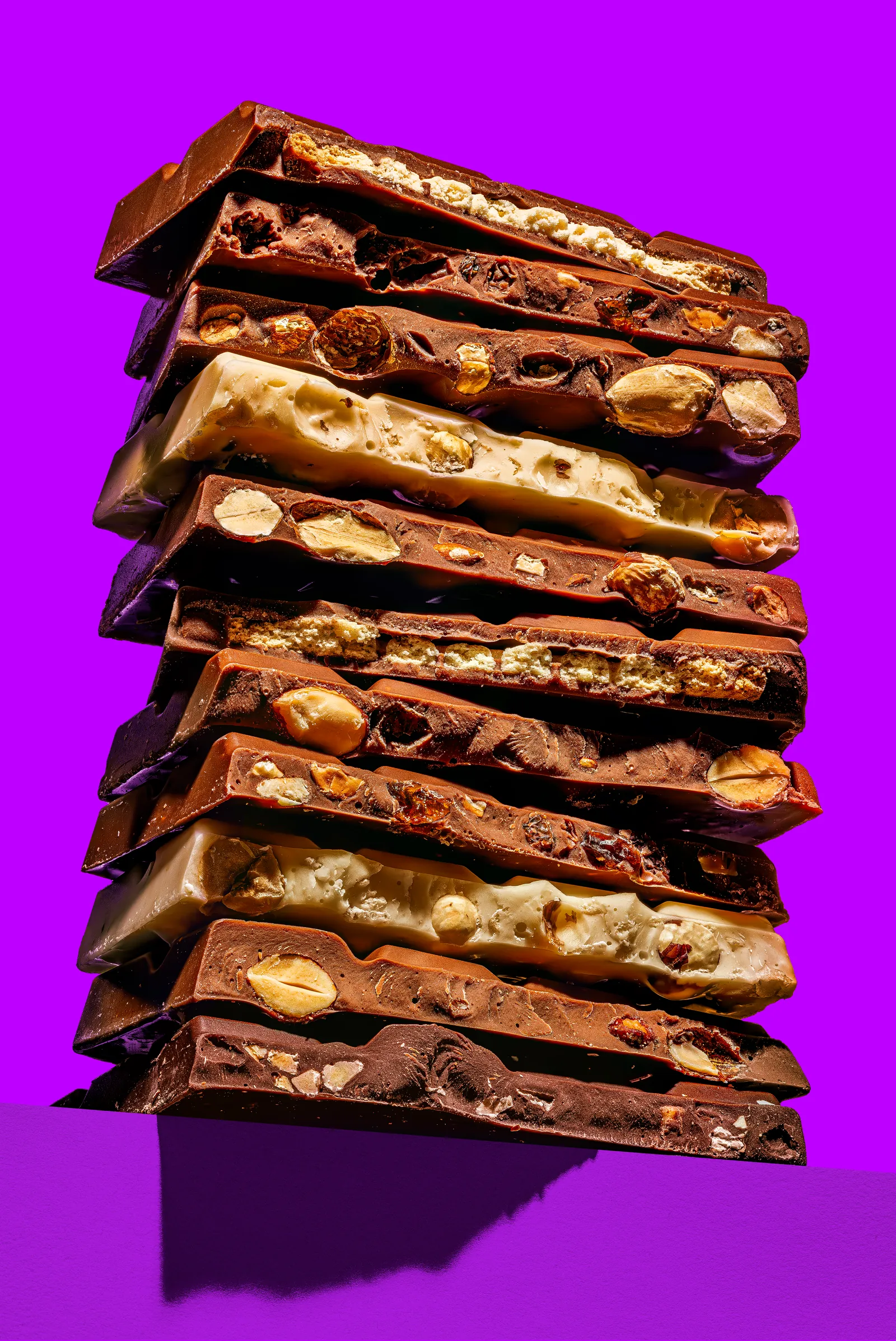 Stack of broken chocolate bars with nuts on a purple background