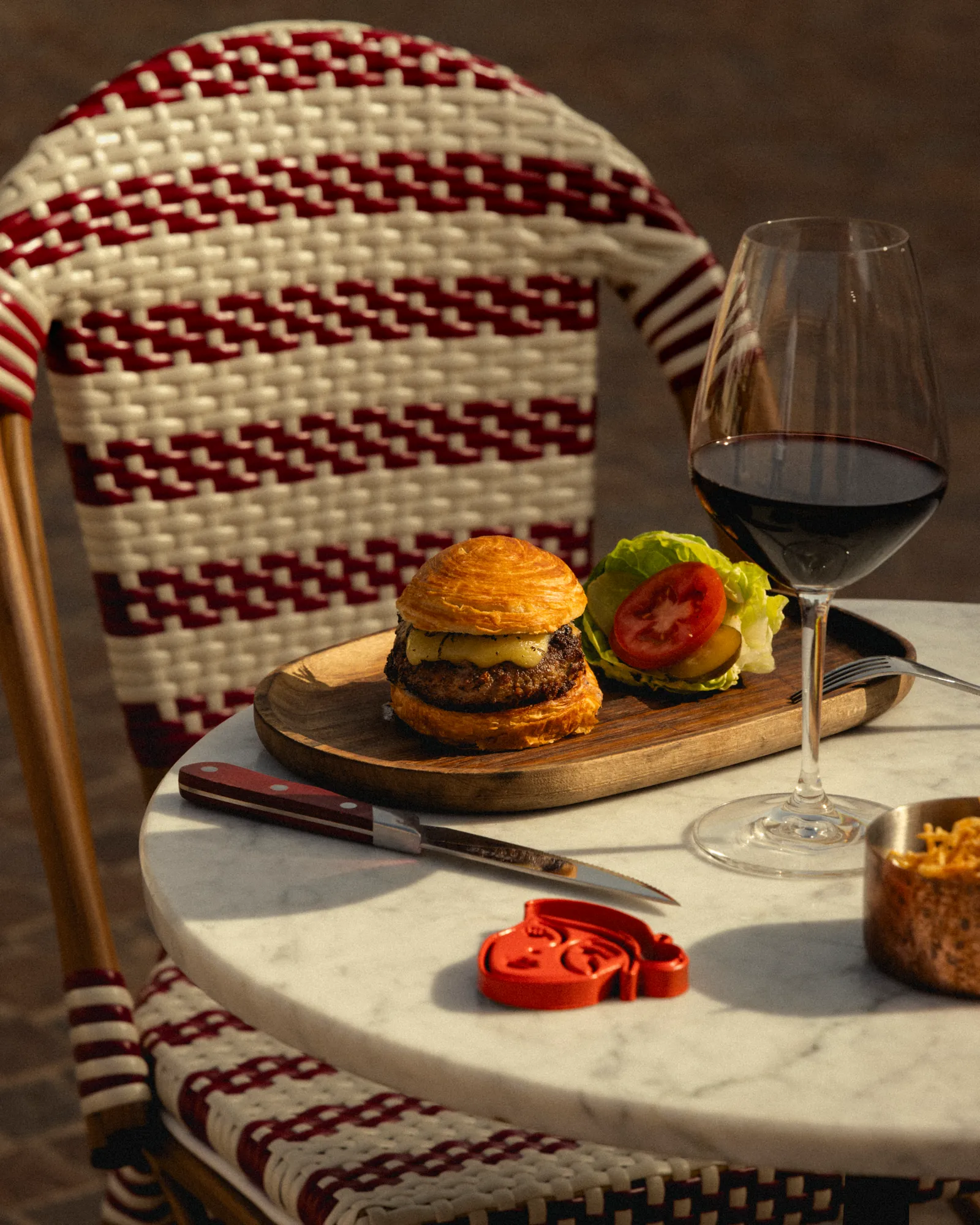 Burger and a glass of red wine on a café table with rattan chairs