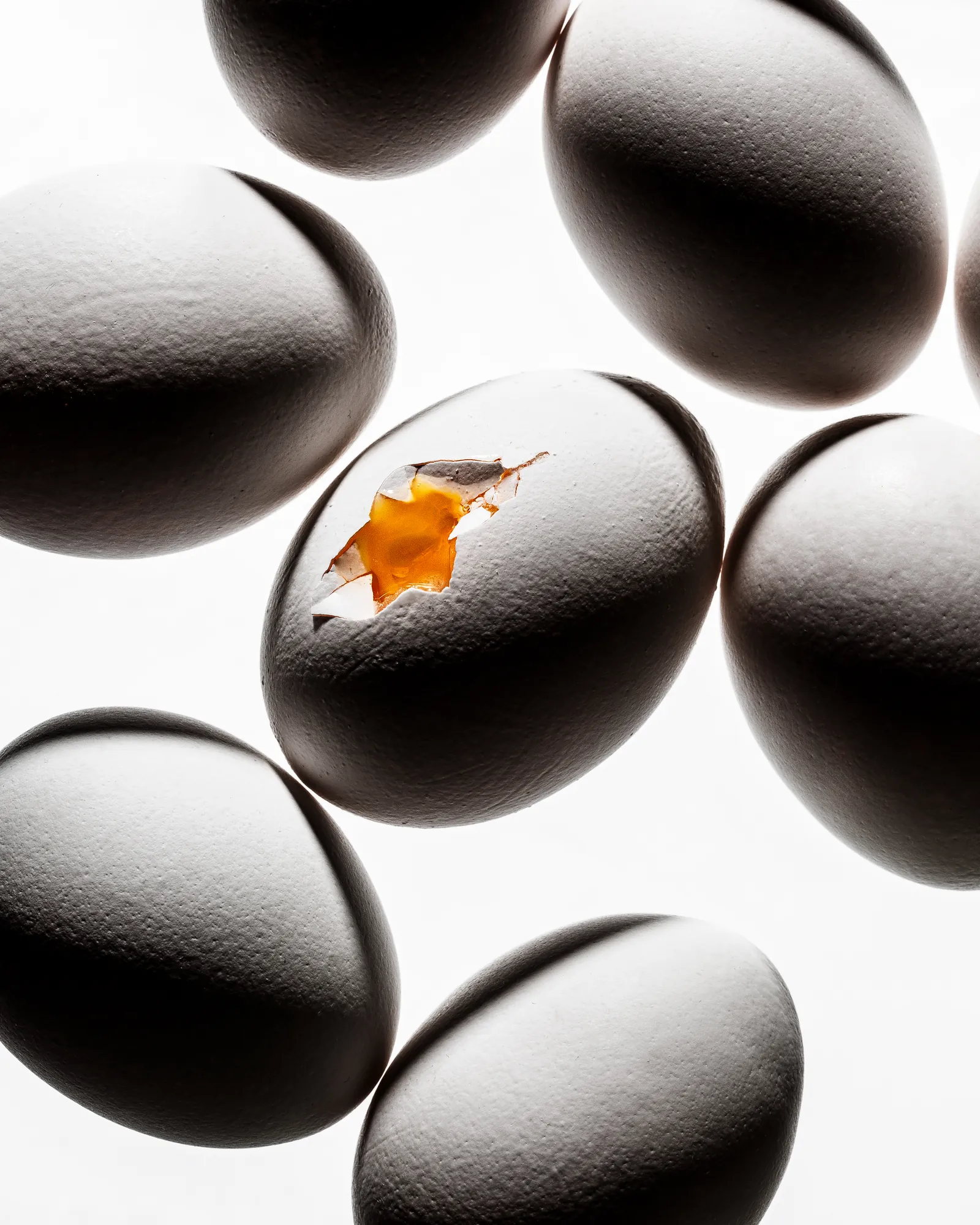 Dark glossy eggs on a white surface, one cracked to show a yolk