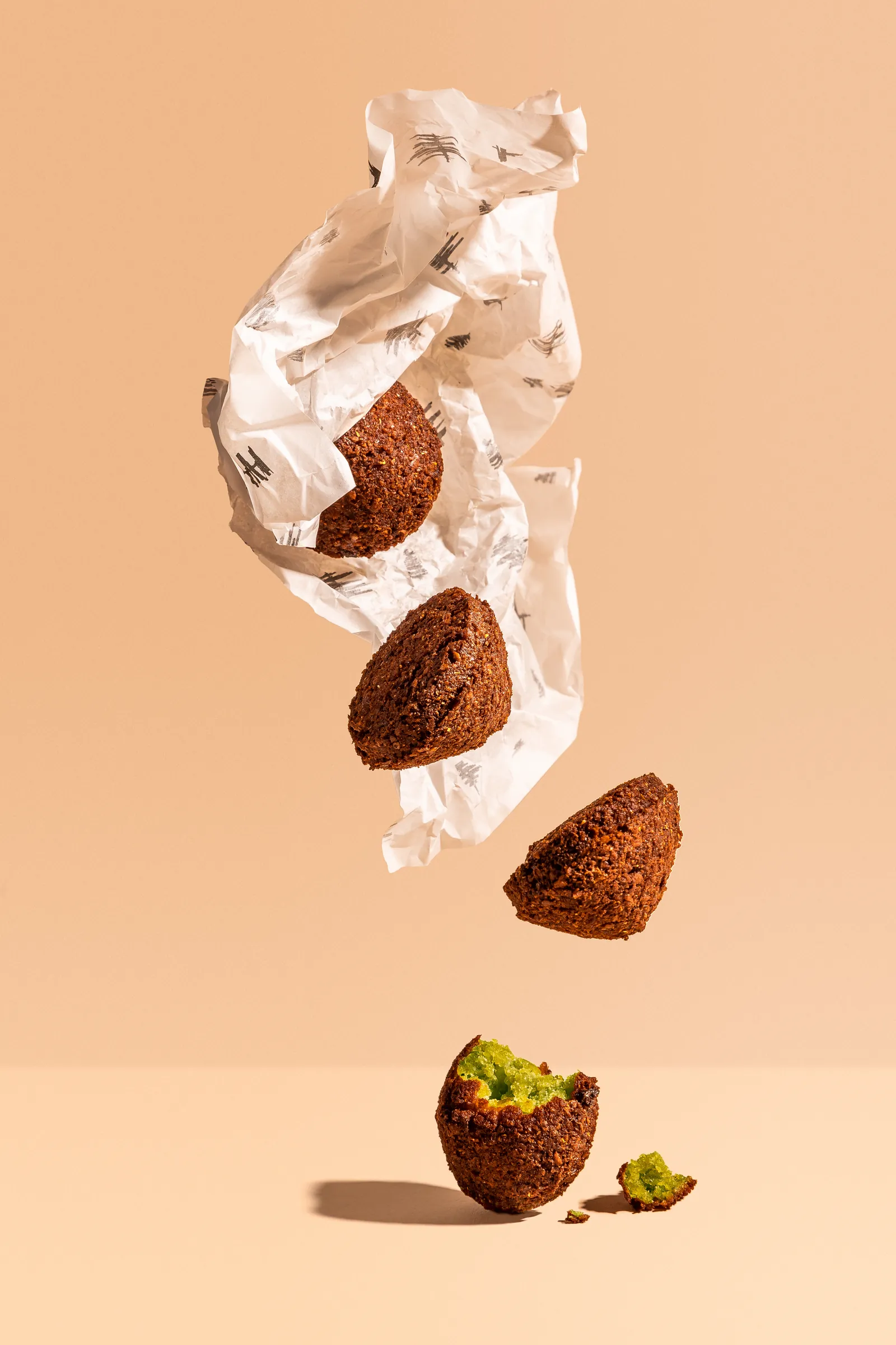 Falafel tumbling out of printed paper wrap on peach, for Baba Lebanese Street Food
