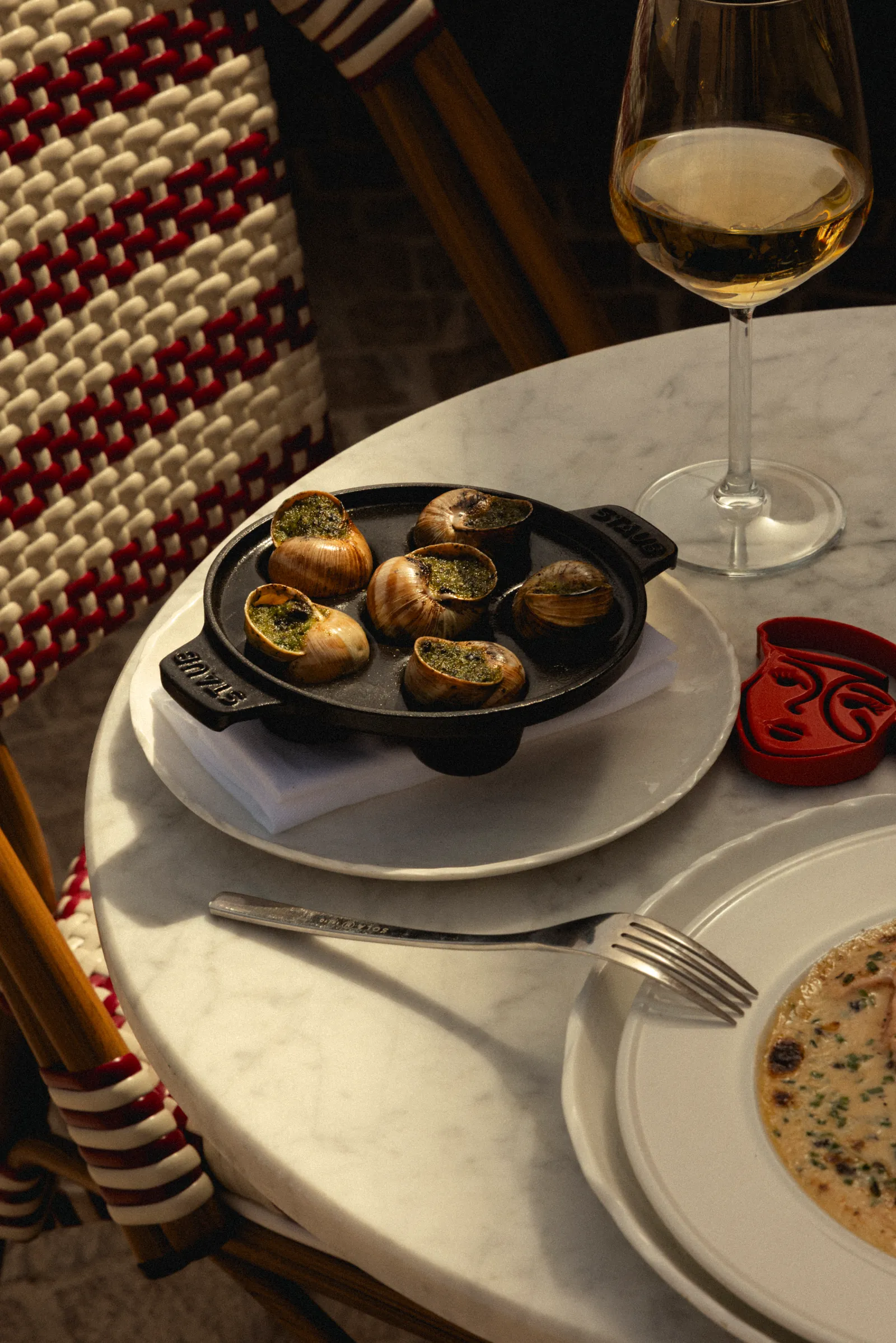 Pan of baked shellfish on a café table beside a glass of white wine