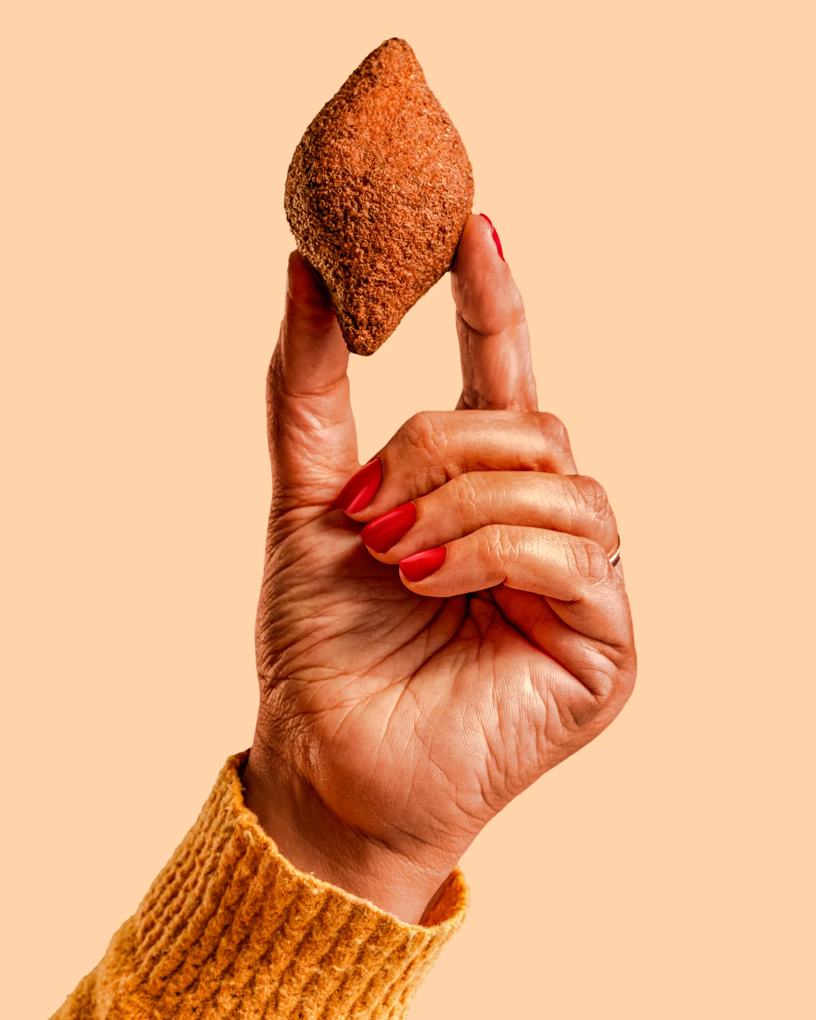 Hand holding a golden fried croquette against a peach background