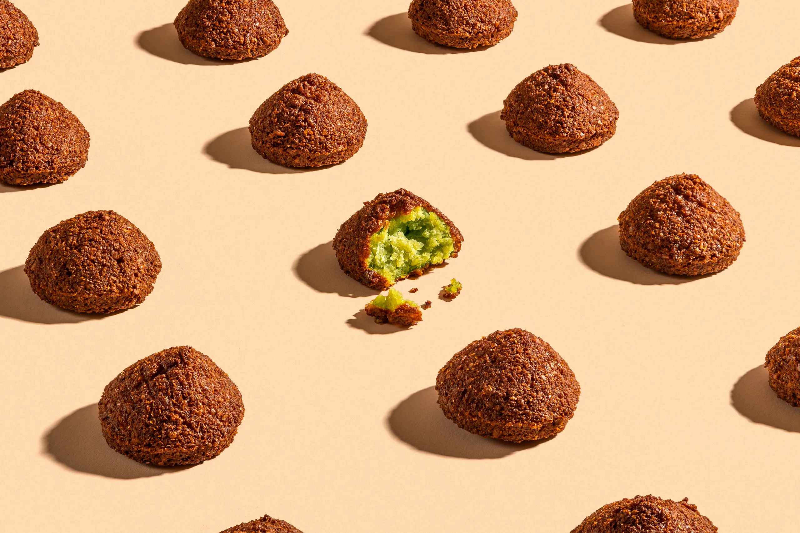 Falafel balls scattered on peach, one cut open to show a green centre