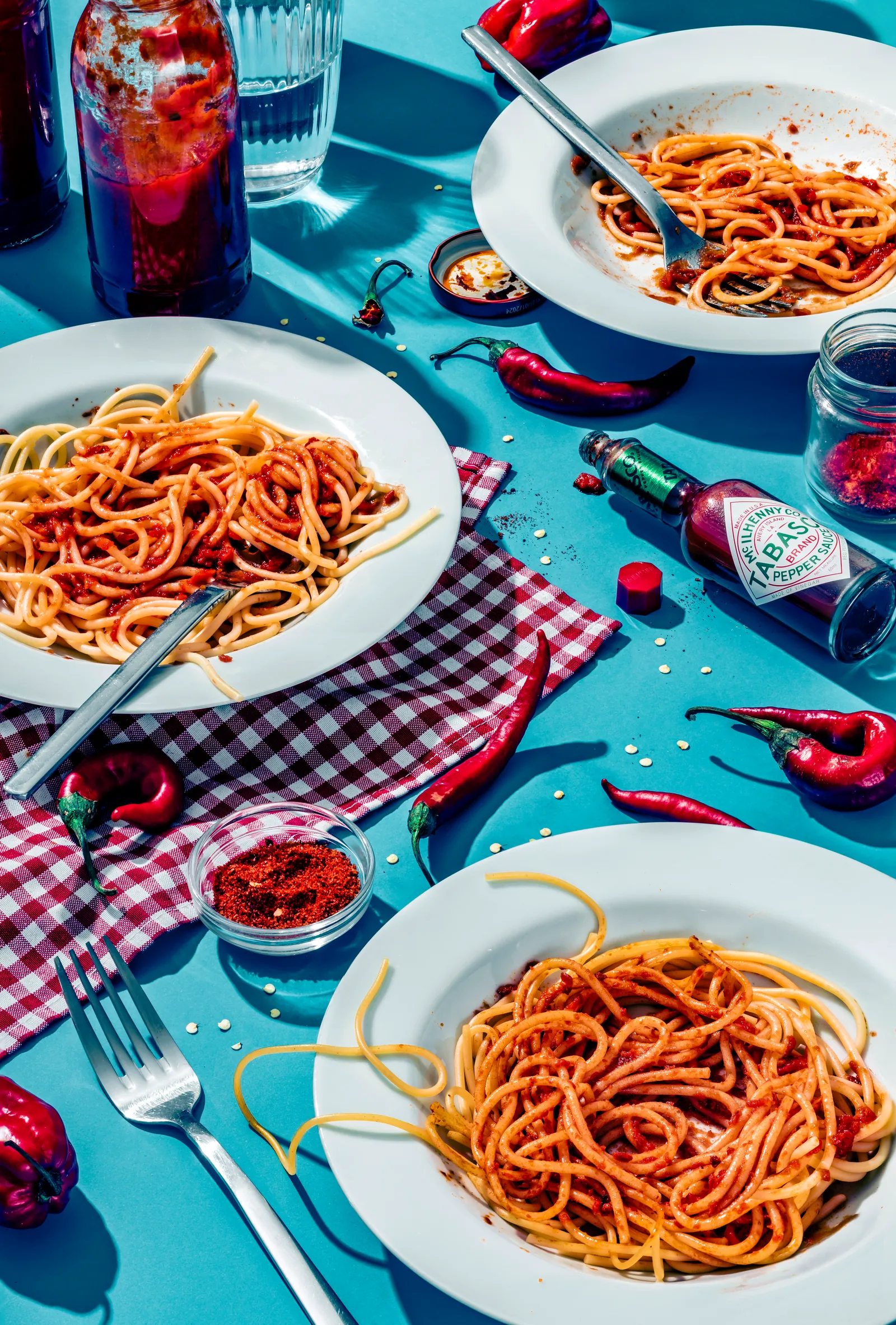 Two plates of spaghetti on a blue table with a red gingham cloth