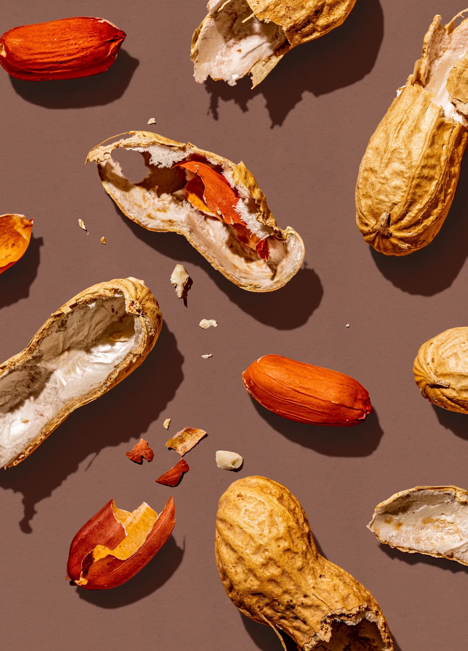 Peanuts and broken shells scattered on a brown background