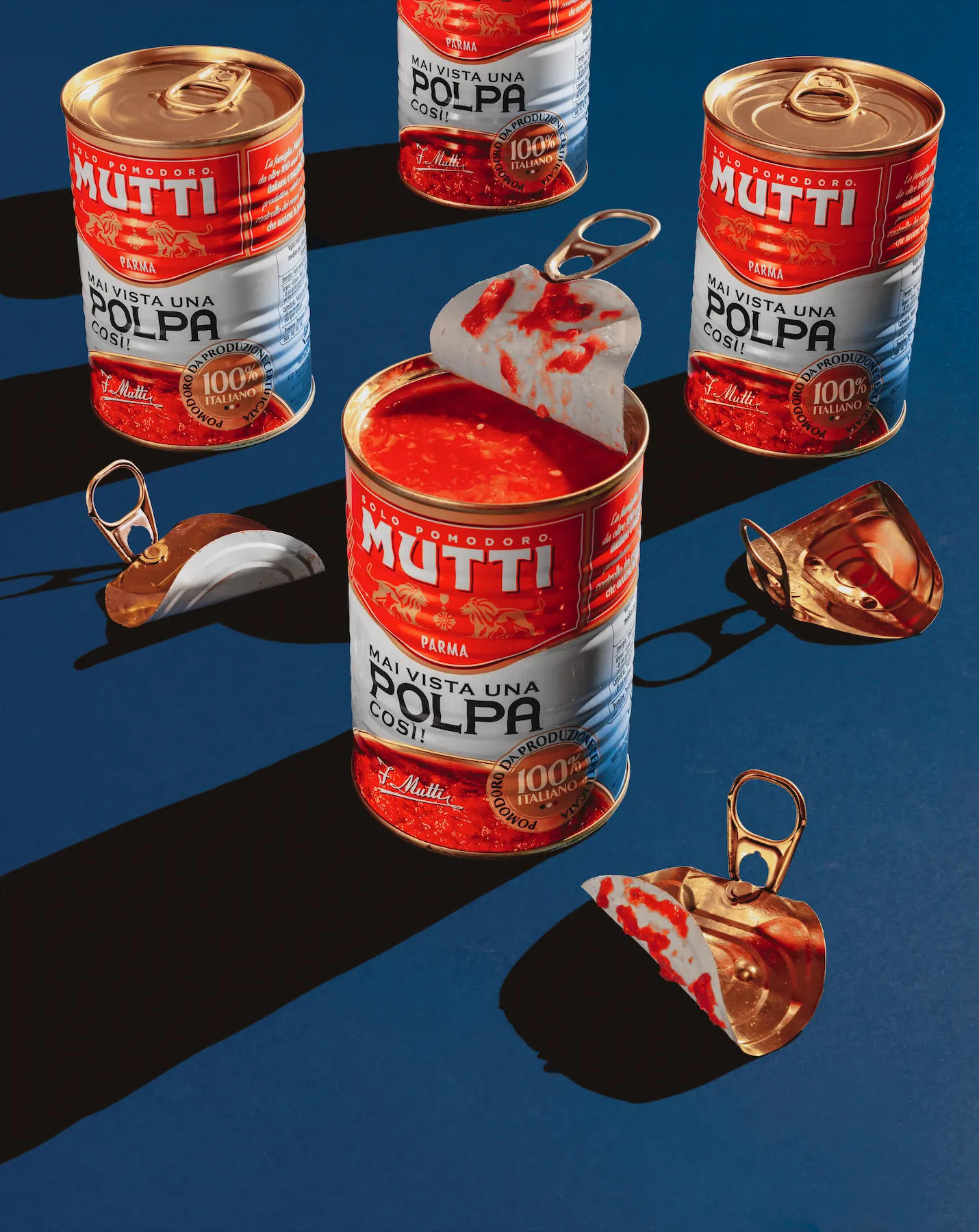 Tins of tomatoes with one split open, on a blue surface