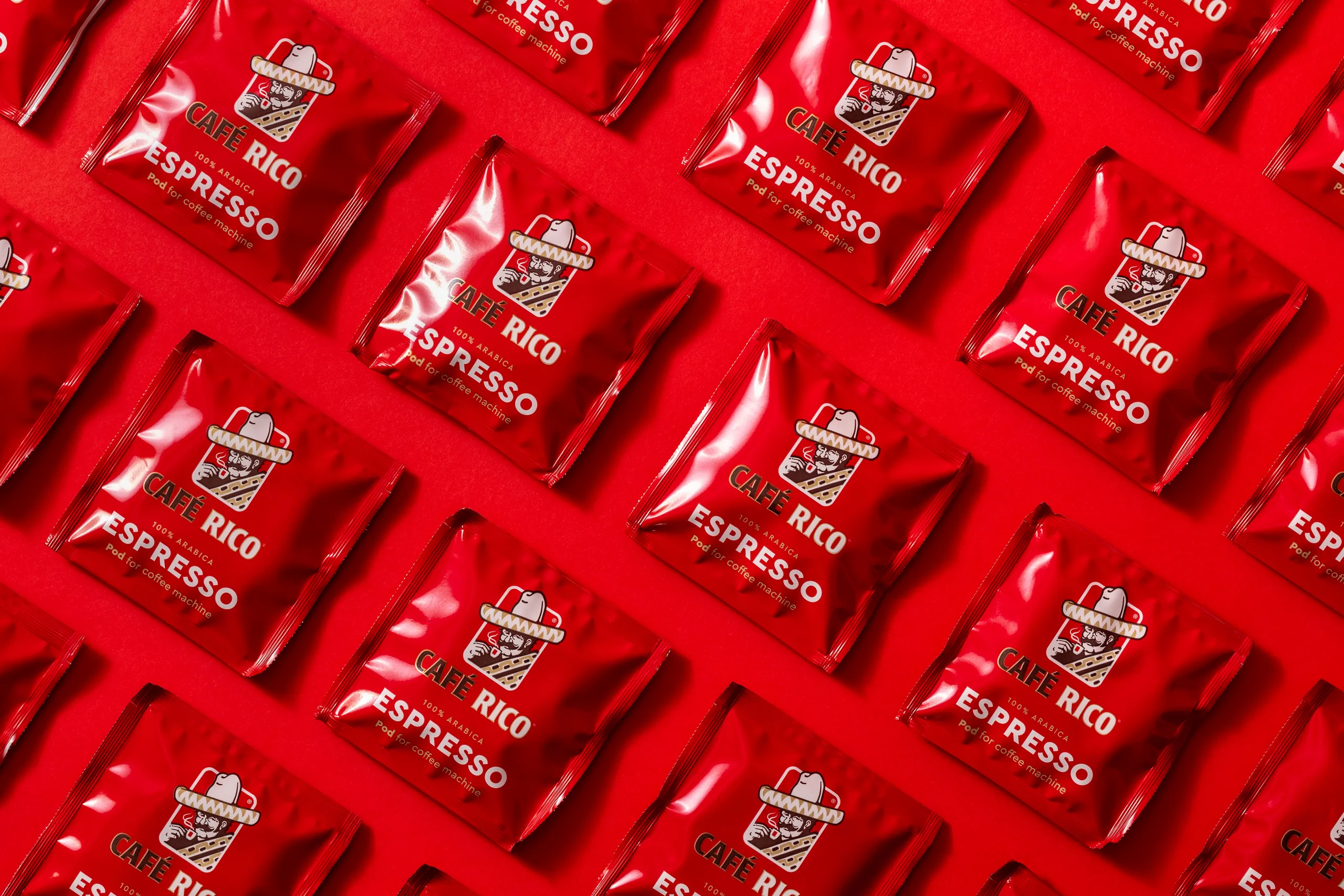 Café Rico coffee pod sachets repeated in diagonal rows on a red background