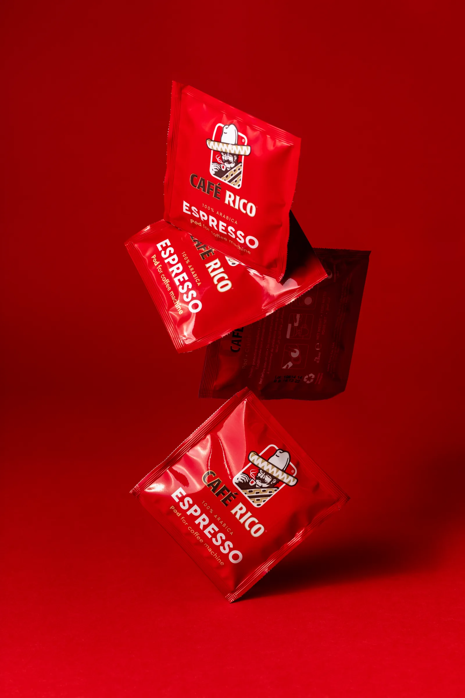 Café Rico coffee pod sachets hanging in mid-air against a red background