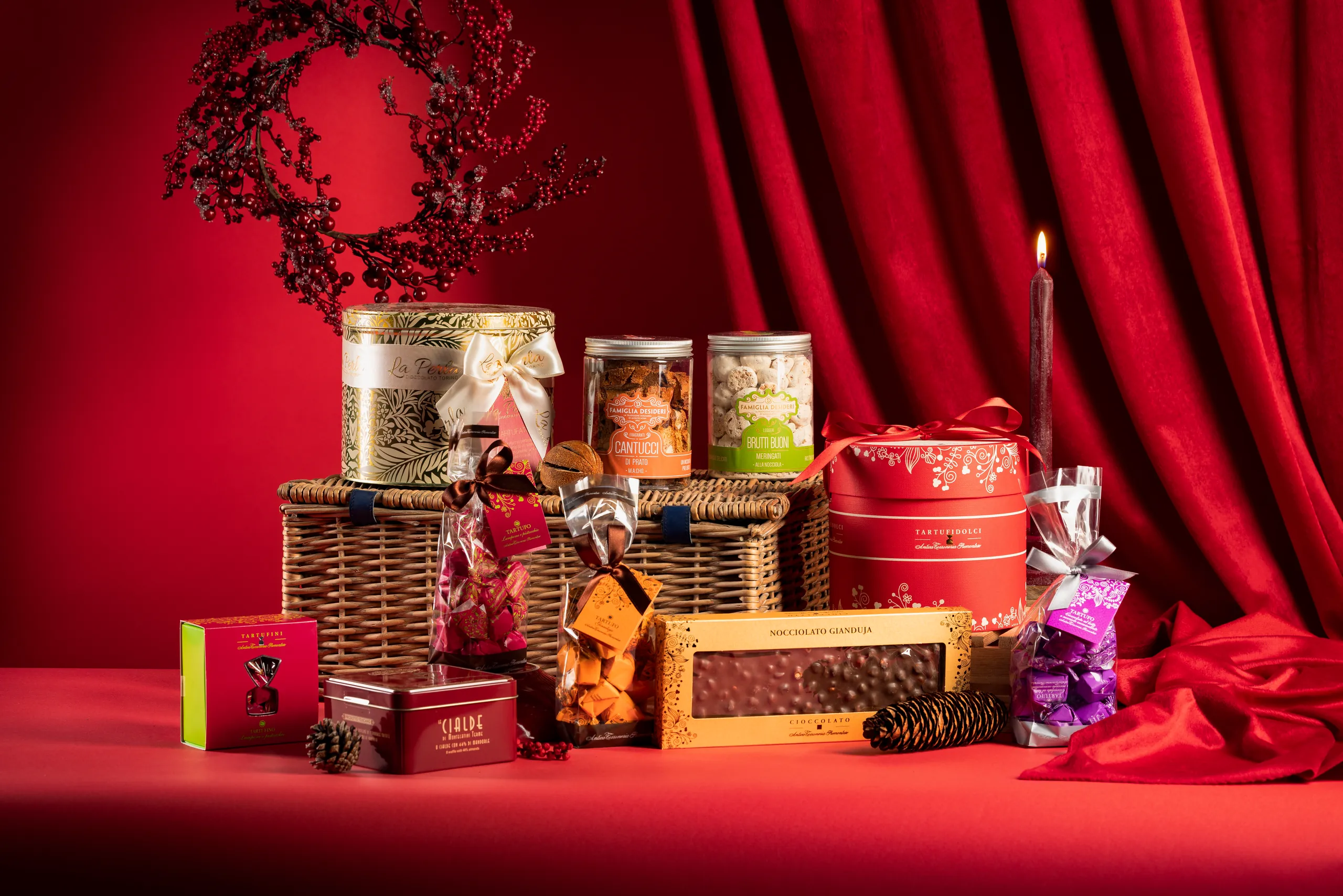 Christmas gift baskets, jars and boxes against a red curtain with a wreath above