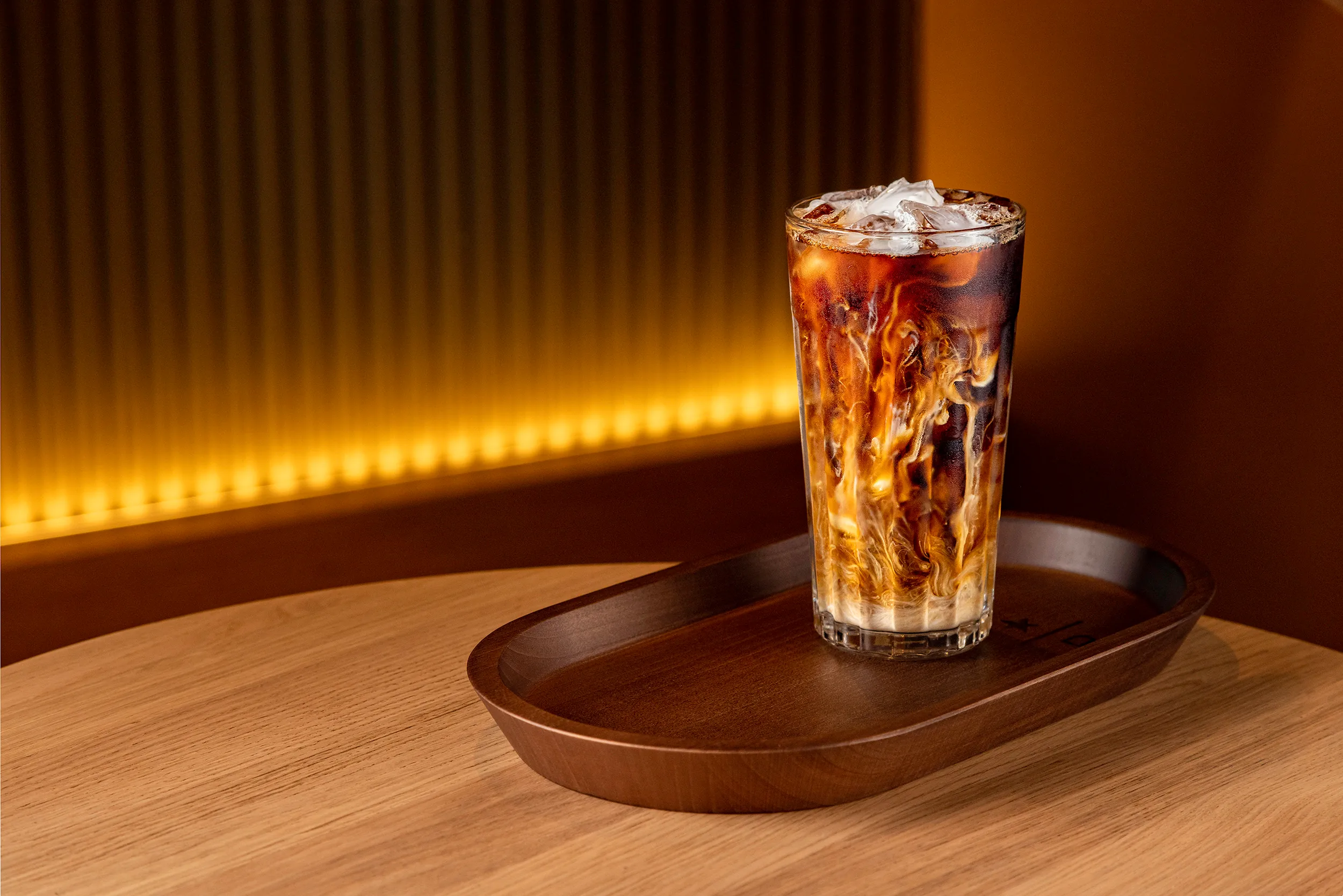 Iced coffee in a tall glass on a wooden tray under warm light