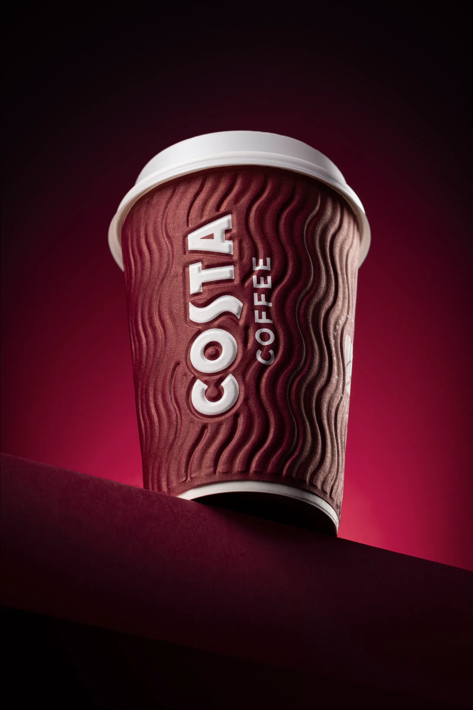 Costa takeaway coffee cup on a dark burgundy surface