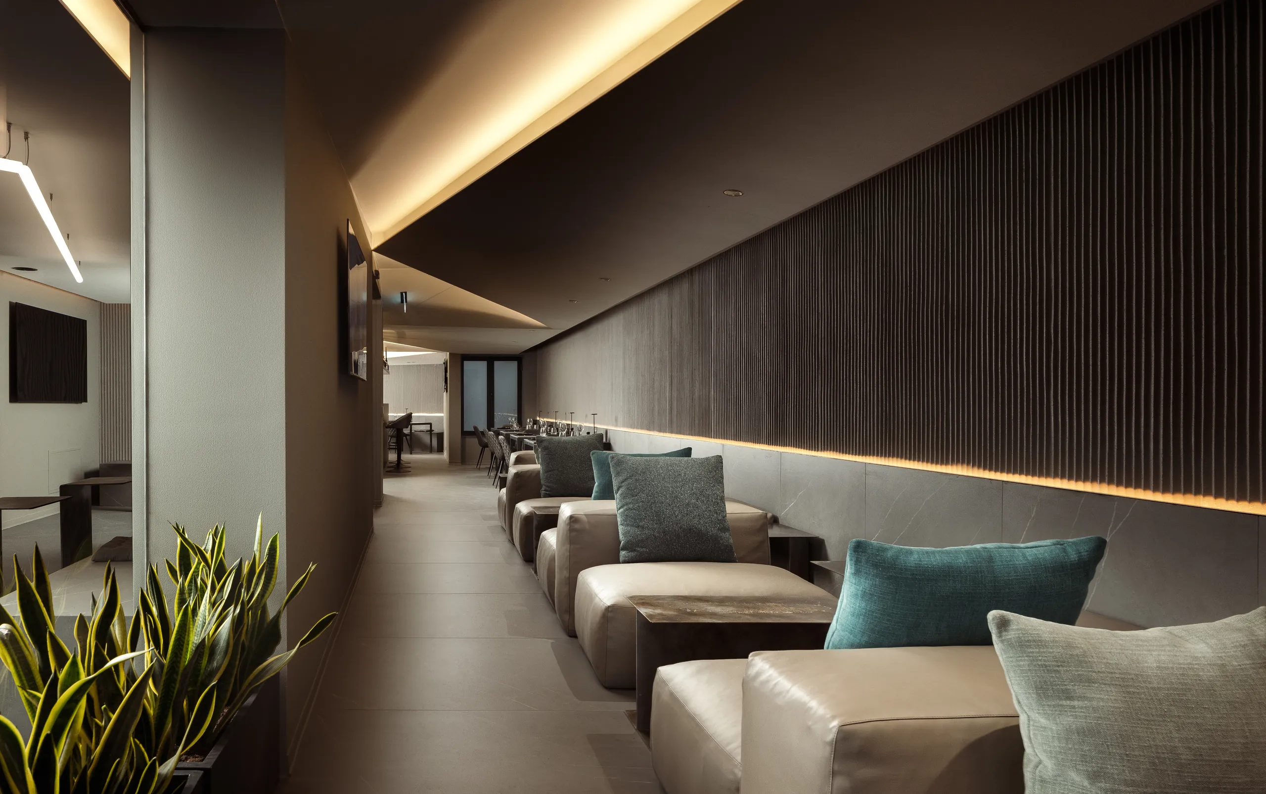 Dark lobby lounge at 33 Boutique Hotel with taupe sofas, teal cushions and a slatted wall lit by warm cove lighting