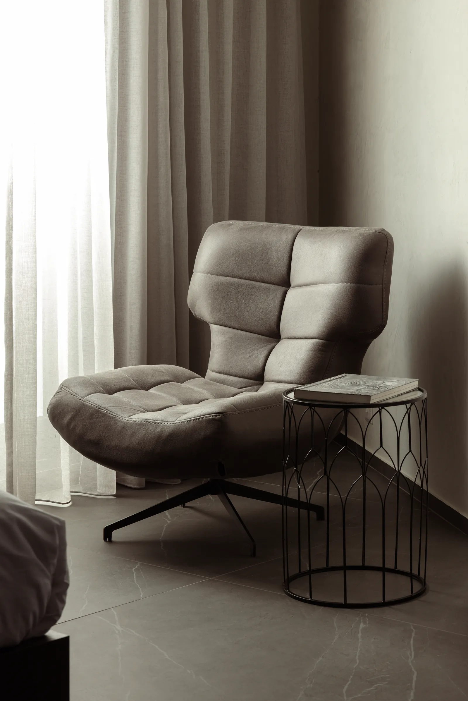 Grey leather armchair and a wire side table by a curtain