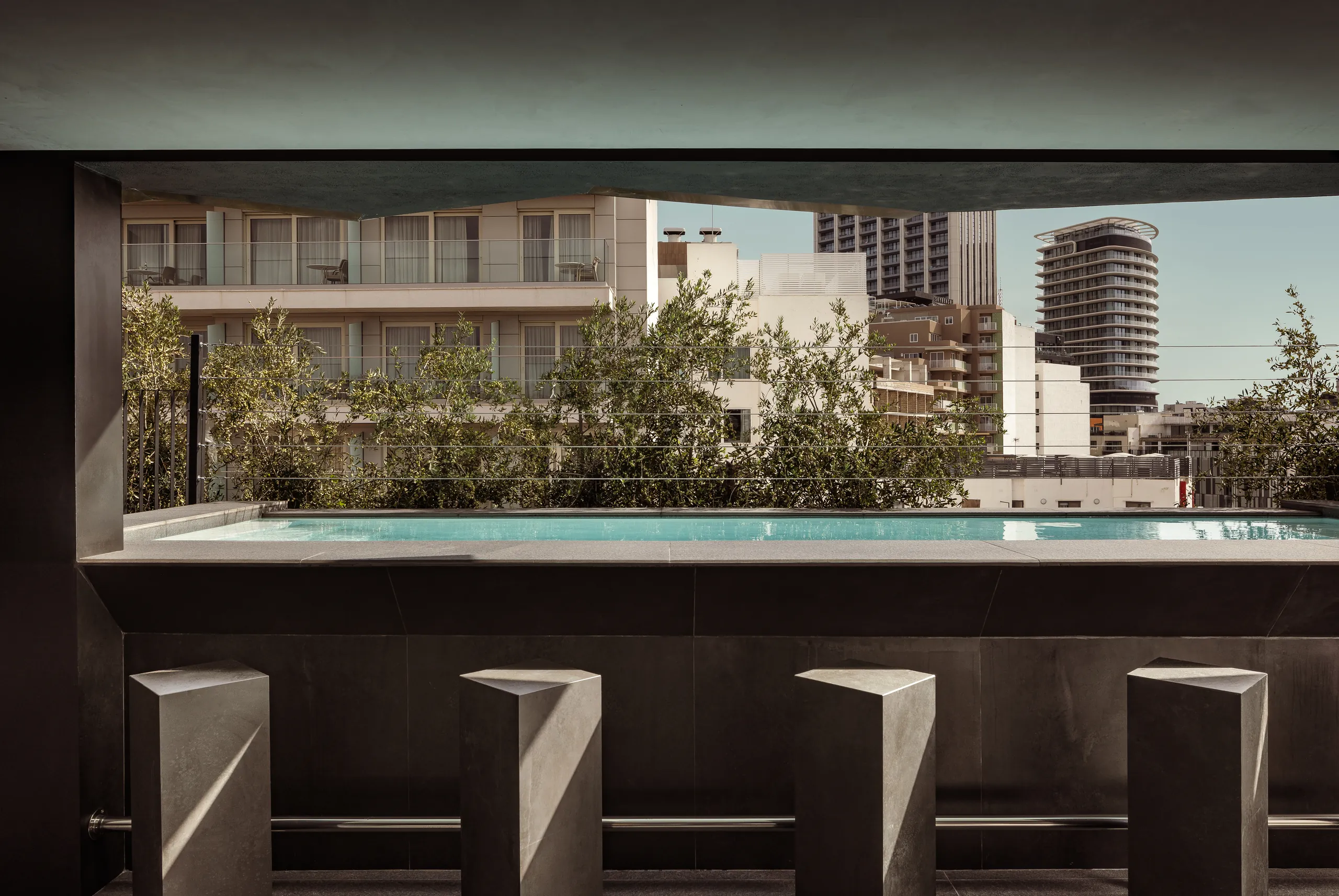 Rooftop pool at 33 Boutique Hotel seen from the bar, with stools and city buildings beyond