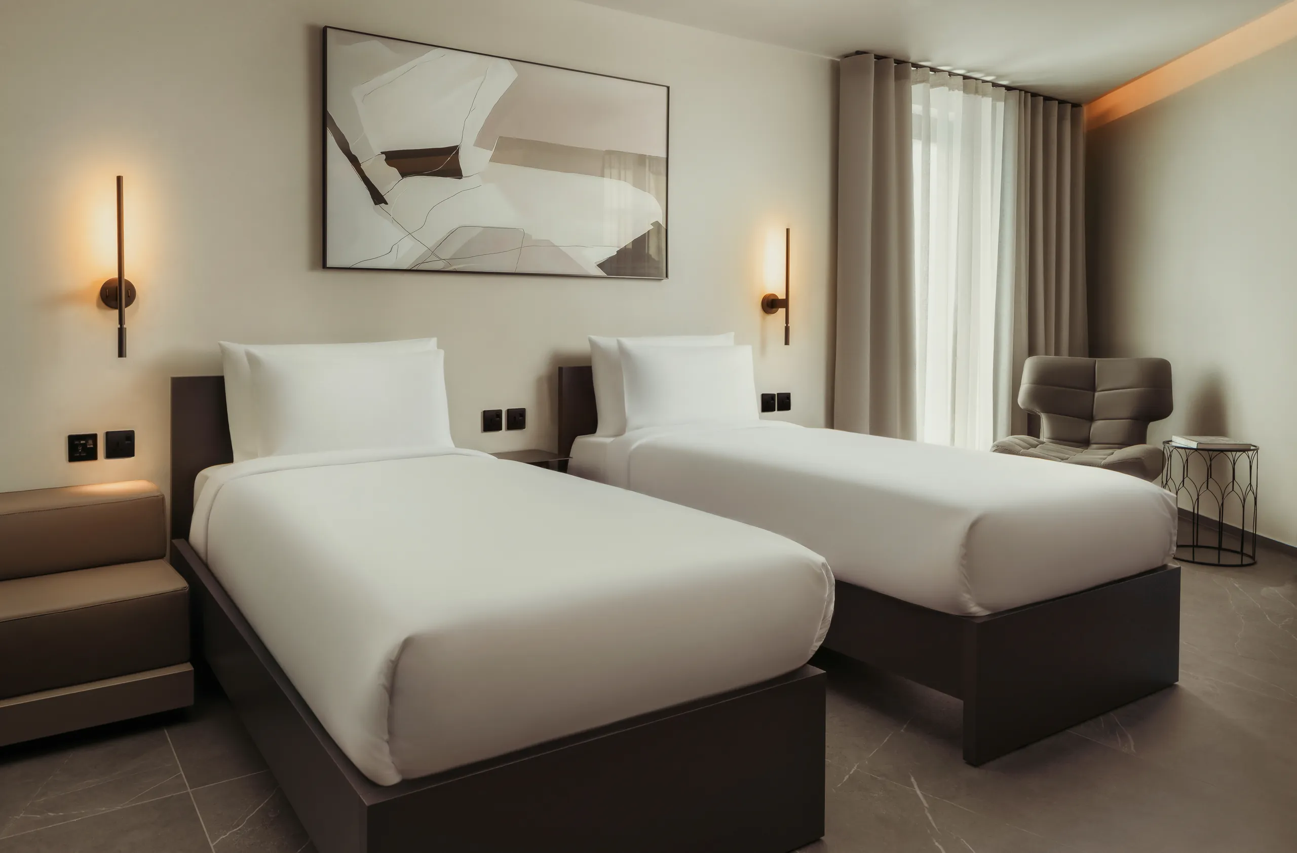 Premium twin hotel room with two white beds, an armchair and abstract artwork
