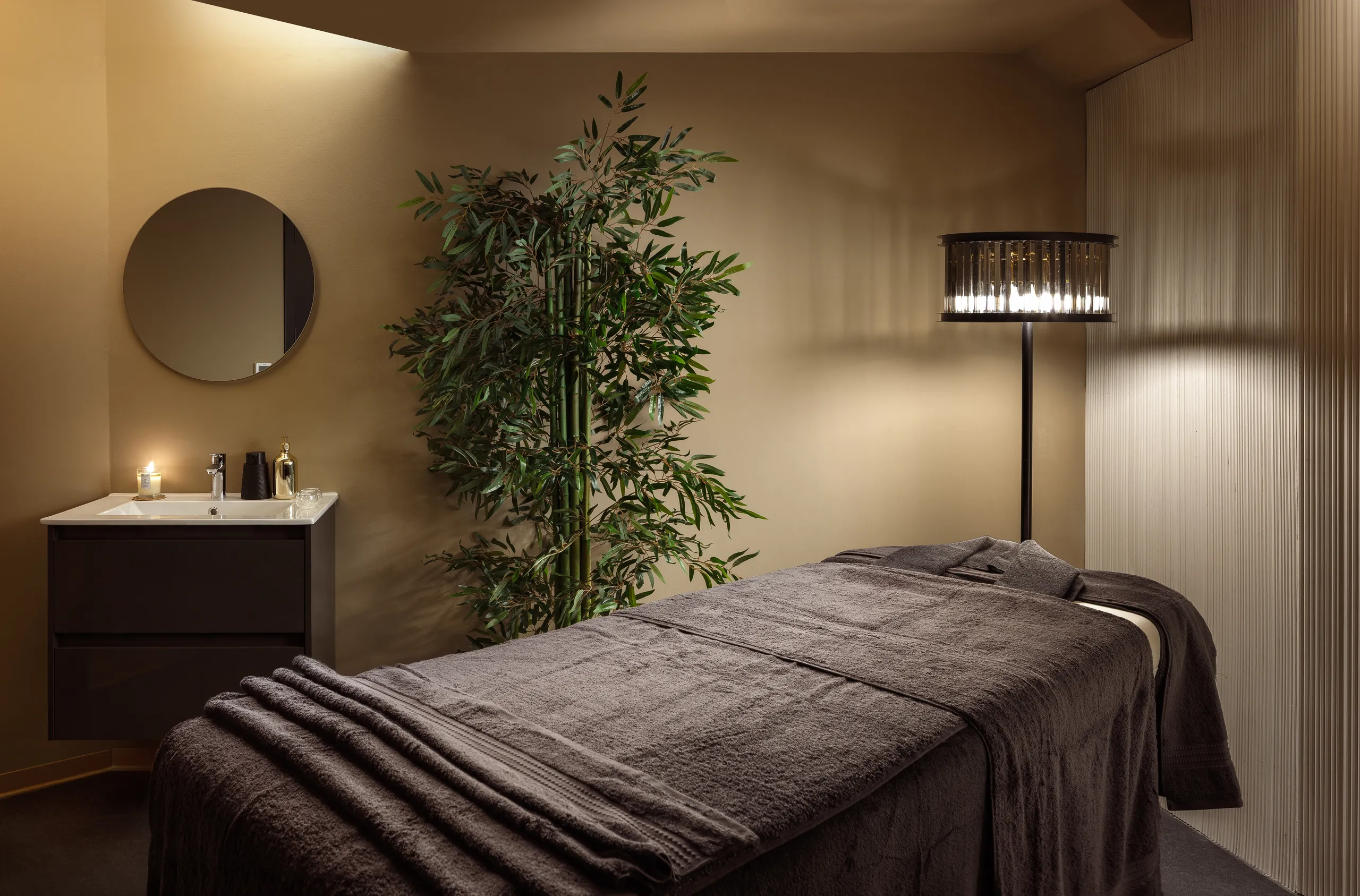 Spa treatment room with a massage bed, a round mirror and a floor lamp