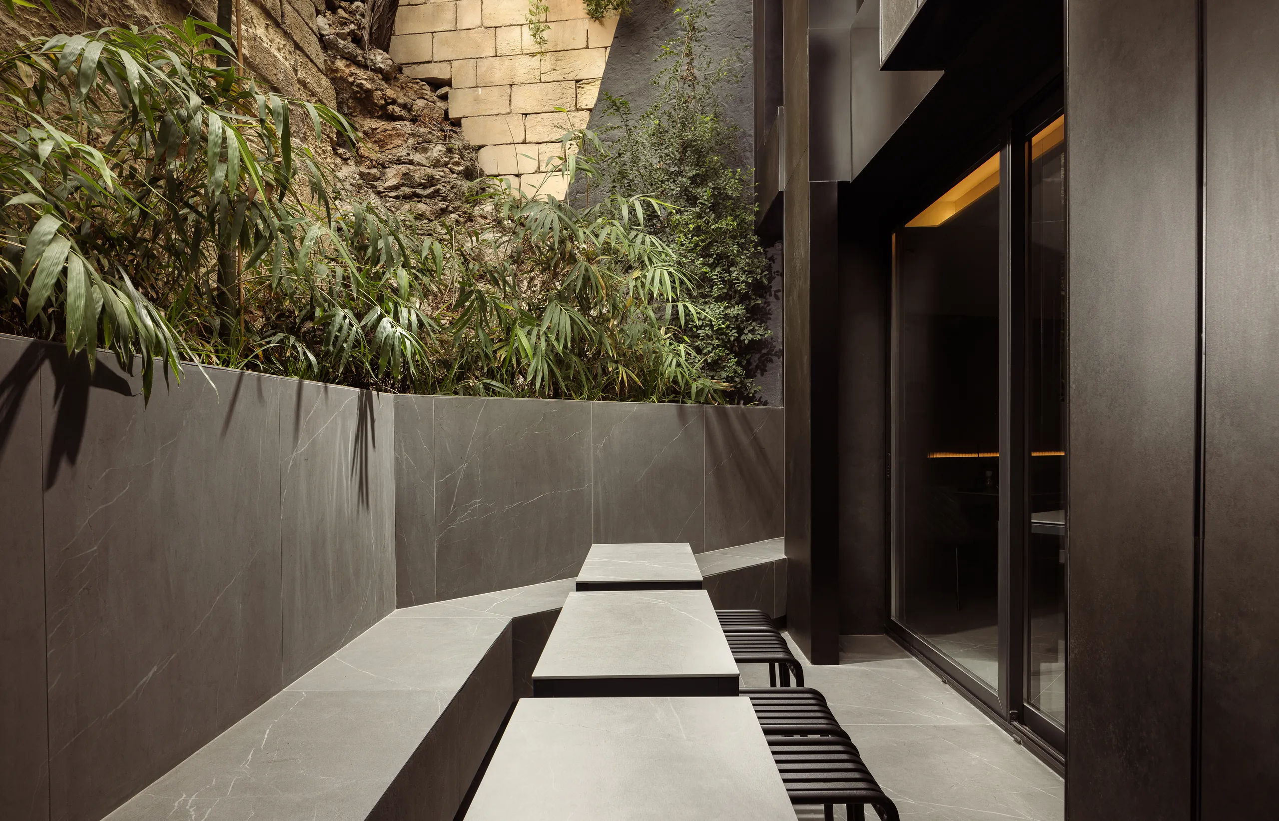 Courtyard with a planted rock wall, a long bench and glass doors